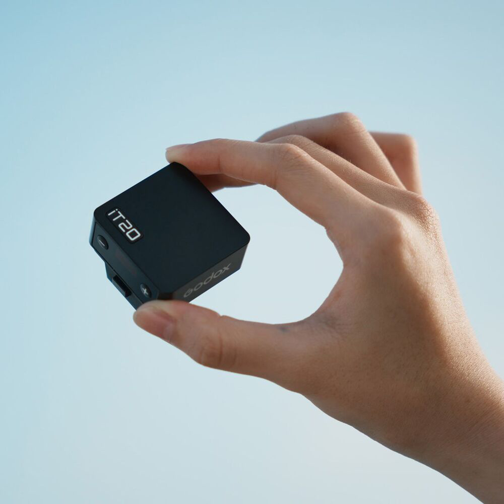 Eine Hand hält ein schwarzes Godox IT20-Gerät vor blauem Himmel. Das Gerät hat einen Bildschirm mit Text.