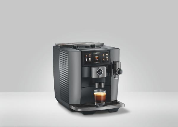 Moderne graue Kaffeemaschine mit einem Glas Espresso auf weißer Oberfläche. Die Maschine hat ein Digitaldisplay.