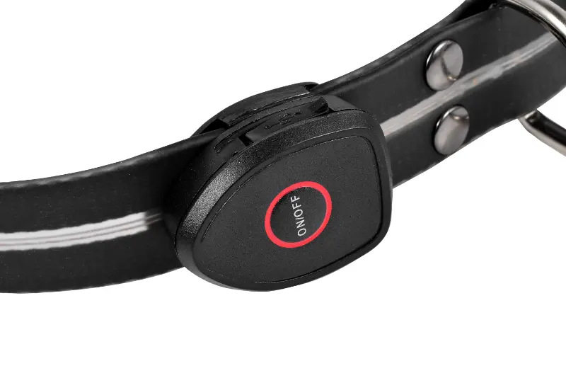 Zbliżenie czarnej obroży dla psa z przyciskiem ON/OFF. Obroża ma biały pasek i metalowy pierścień.