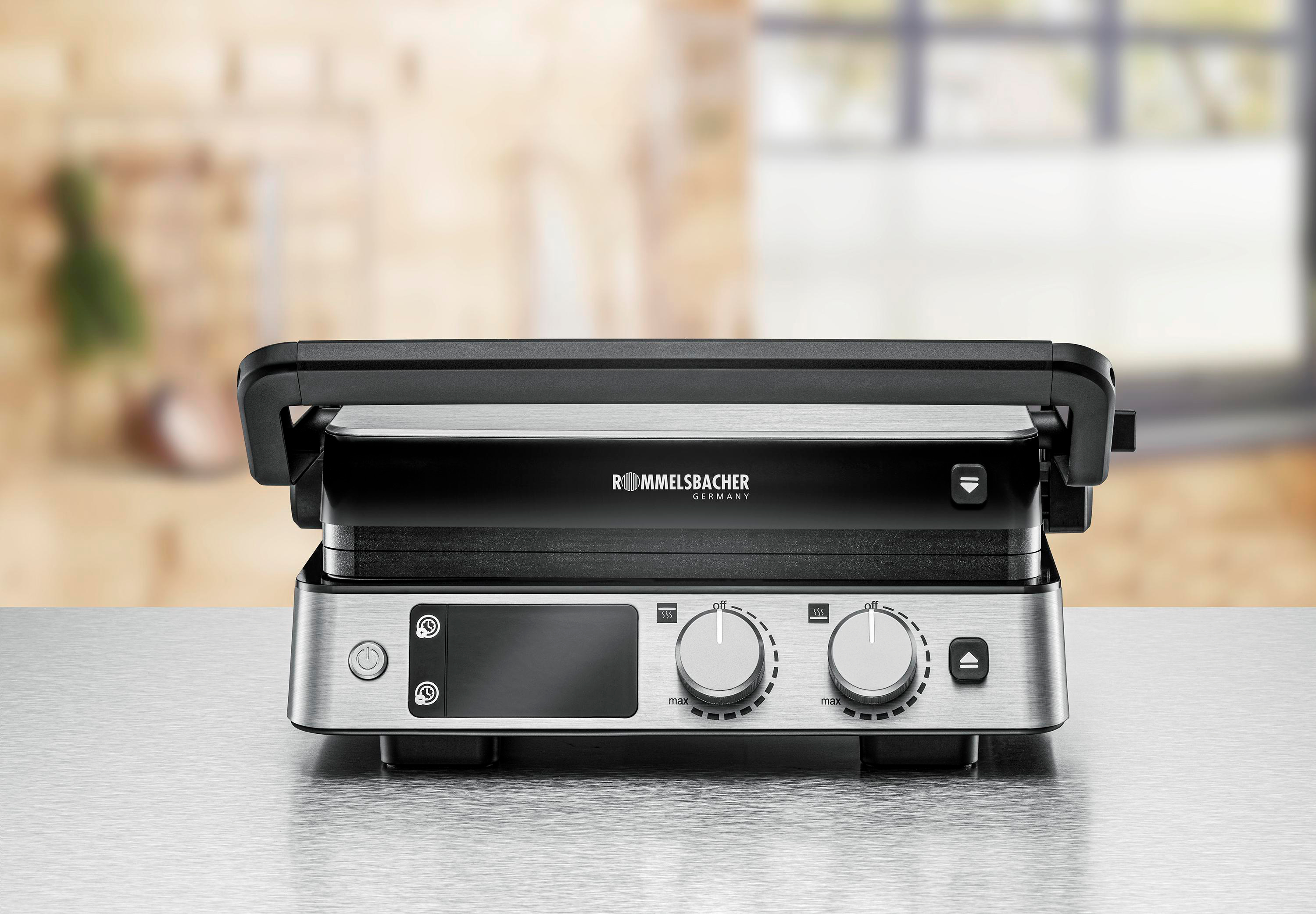 Ein silberner Grill mit schwarzer Oberseite. Es hat Drehregler und ein digitales Display. Der Hintergrund ist unscharf.