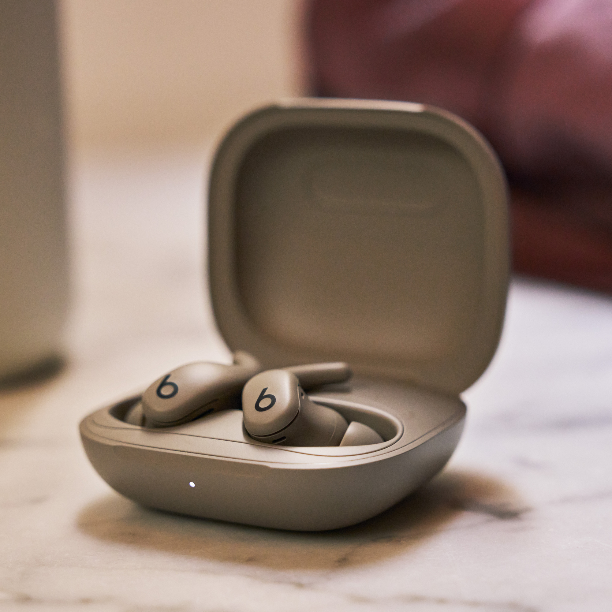 Beats-Ohrhörer in ihrem offenen Gehäuse. Das Gehäuse und die Ohrhörer sind beige. Der Hintergrund zeigt eine verschwommene Oberfläche und eine hellfarbige Oberfläche.