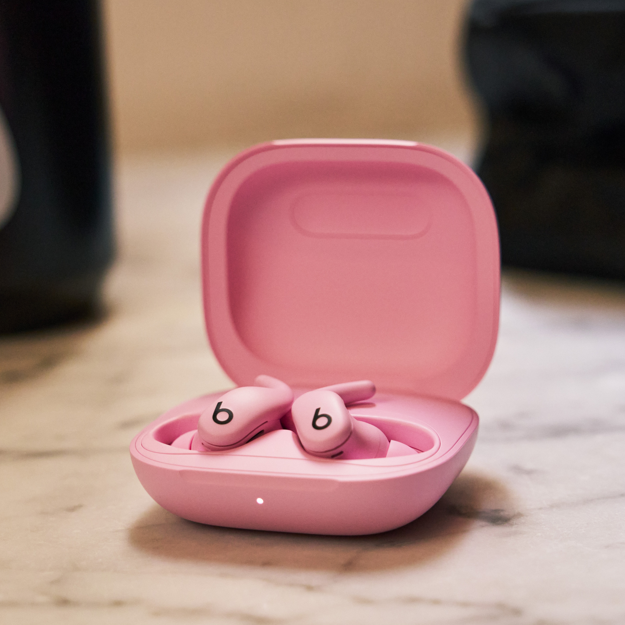 Rosa Beats-Ohrhörer in einem offenen rosa Gehäuse auf einer Marmoroberfläche. Die Ohrhörer haben ein 'b'-Logo.