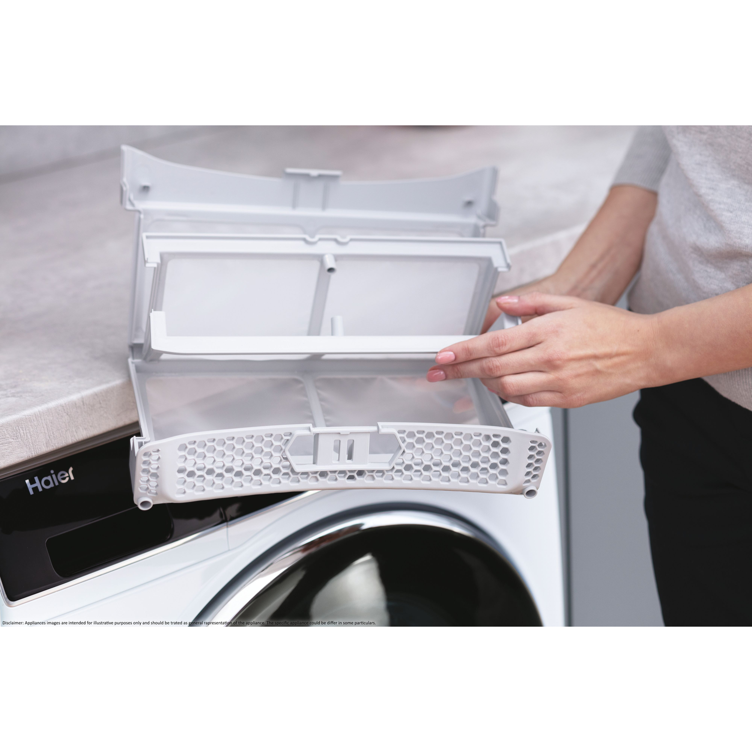 A woman opens a white dryer filter. The dryer is white with a black door and the Haier logo on the front.