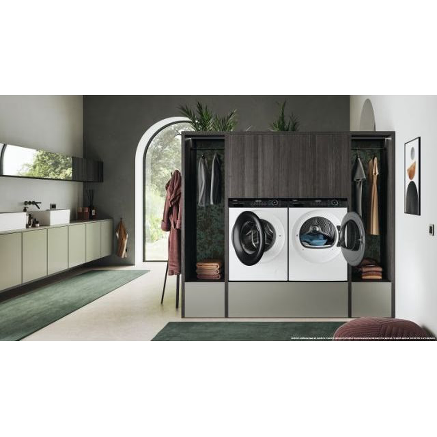 A modern laundry room with washing machines, clothes, and a window. Green rug and cabinets. A bathrobe hangs on a rack.