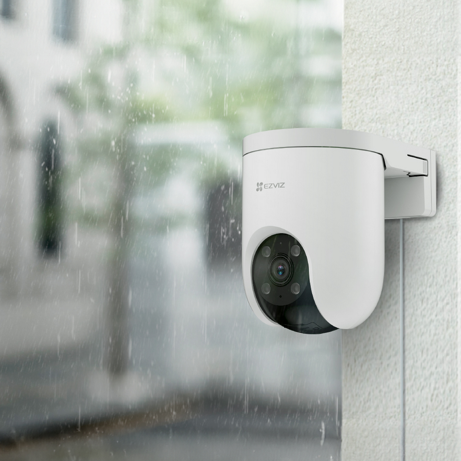 Una cámara de seguridad blanca montada en una pared, con el logotipo de EZVIZ, bajo la lluvia. El fondo muestra una escena callejera borrosa.
