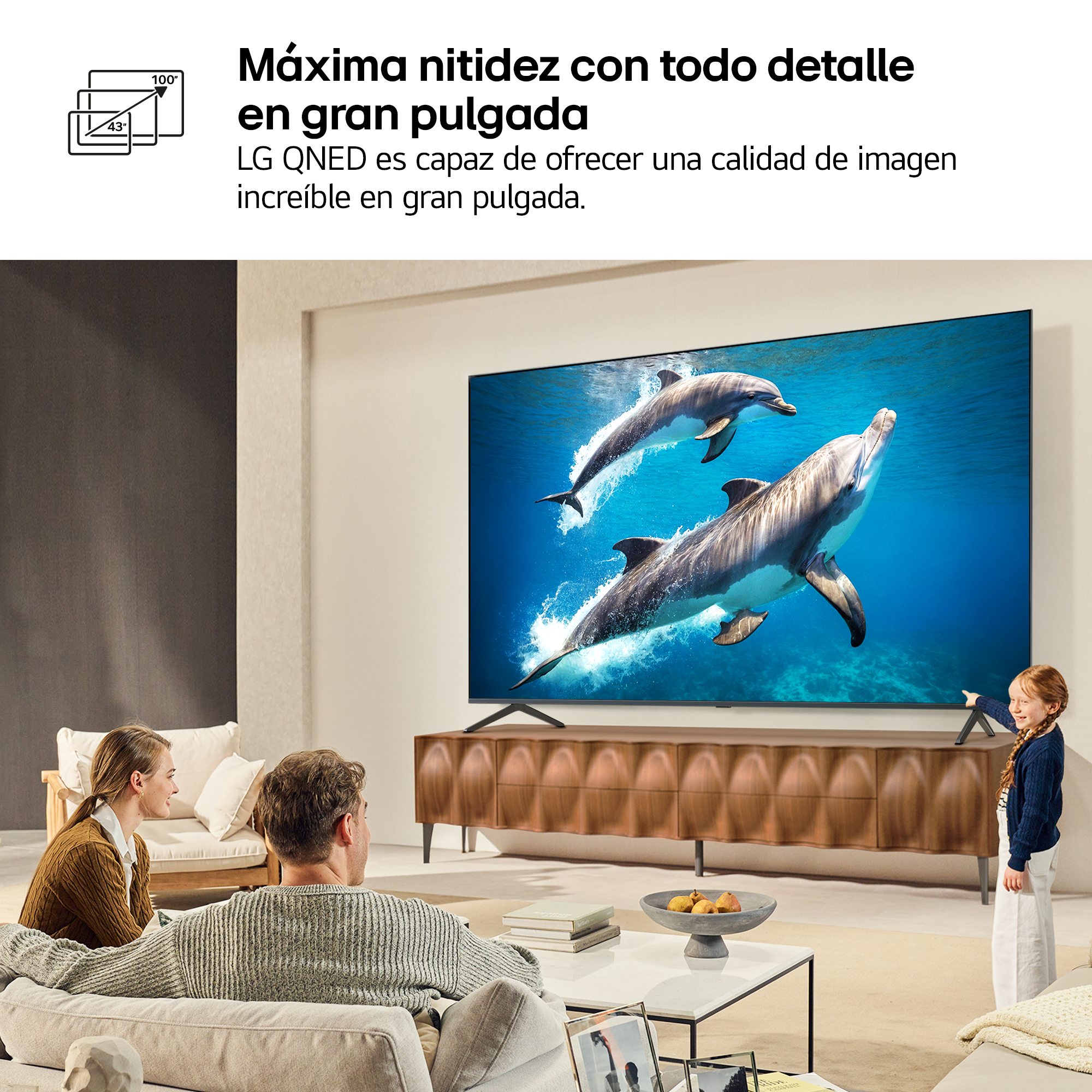 Una familia mira la TV con delfines. Una niña señala la pantalla. La habitación tiene diseño moderno.