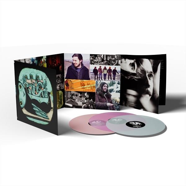Vinyl-Schallplattenset mit Albumcover mit Bandfotos und einem surrealen Bild. Drei Vinyl-Schallplatten in Rosa und Grau sind vorne.