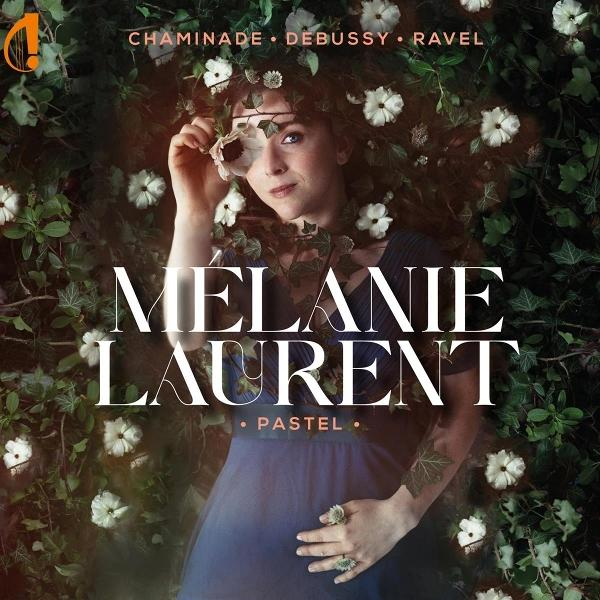 Frau mit Blumenkranz, hält eine Blume, umgeben von Grün und Blumen. Der Name Melanie Laurent wird angezeigt.