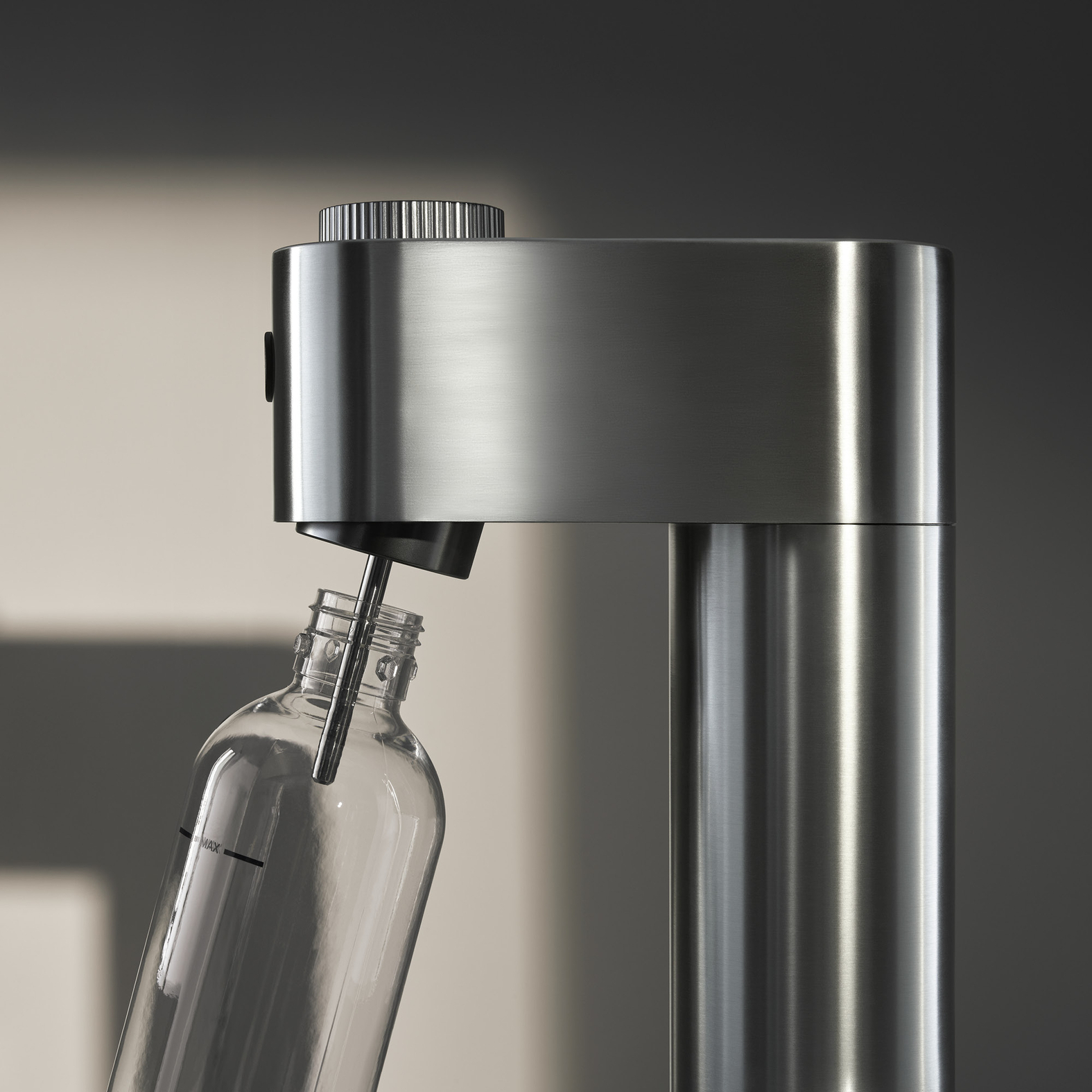 Ein Sodabereiter mit einer Glasflasche. Die Maschine ist silberfarben, die Flasche ist klar. Die Flasche wird gefüllt.