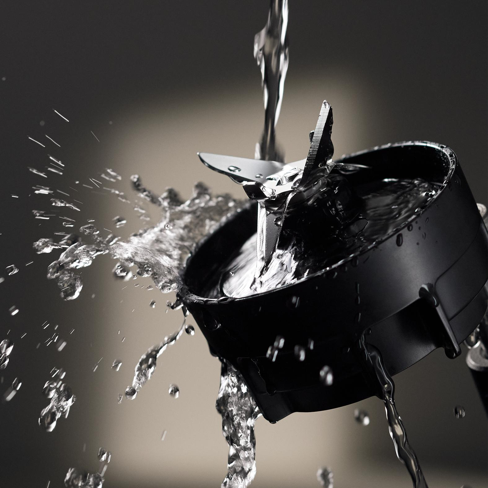 Wasser gießt in einen schwarzen Mixbecher mit Klingen. Wasser spritzt um den Becher herum.