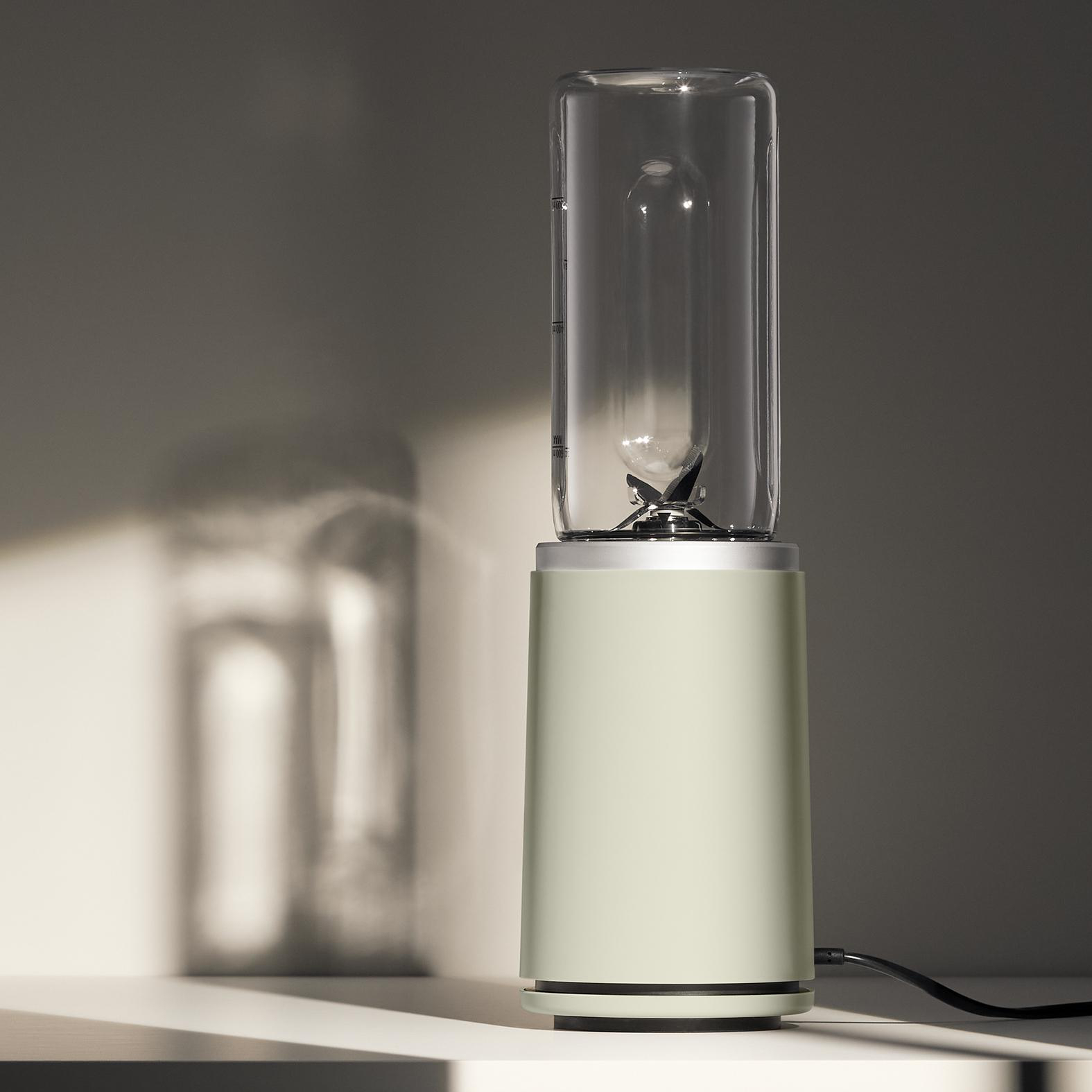 Ein hellgrüner Mixer auf einer weißen Oberfläche mit dunklem Hintergrund. Der Schatten des Mixers ist sichtbar.