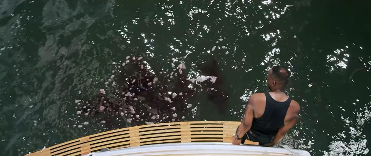 Ein Mann auf einem Boot blickt auf dunkles Wasser mit weißem Schaum. Hölzernes Bootsdeck im Blick.
