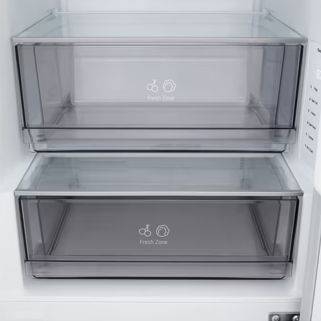 Wewnątrz lodówki widać dwie przezroczyste szuflady z napisem 'Fresh Zone'. Szuflady są puste, na białym tle.