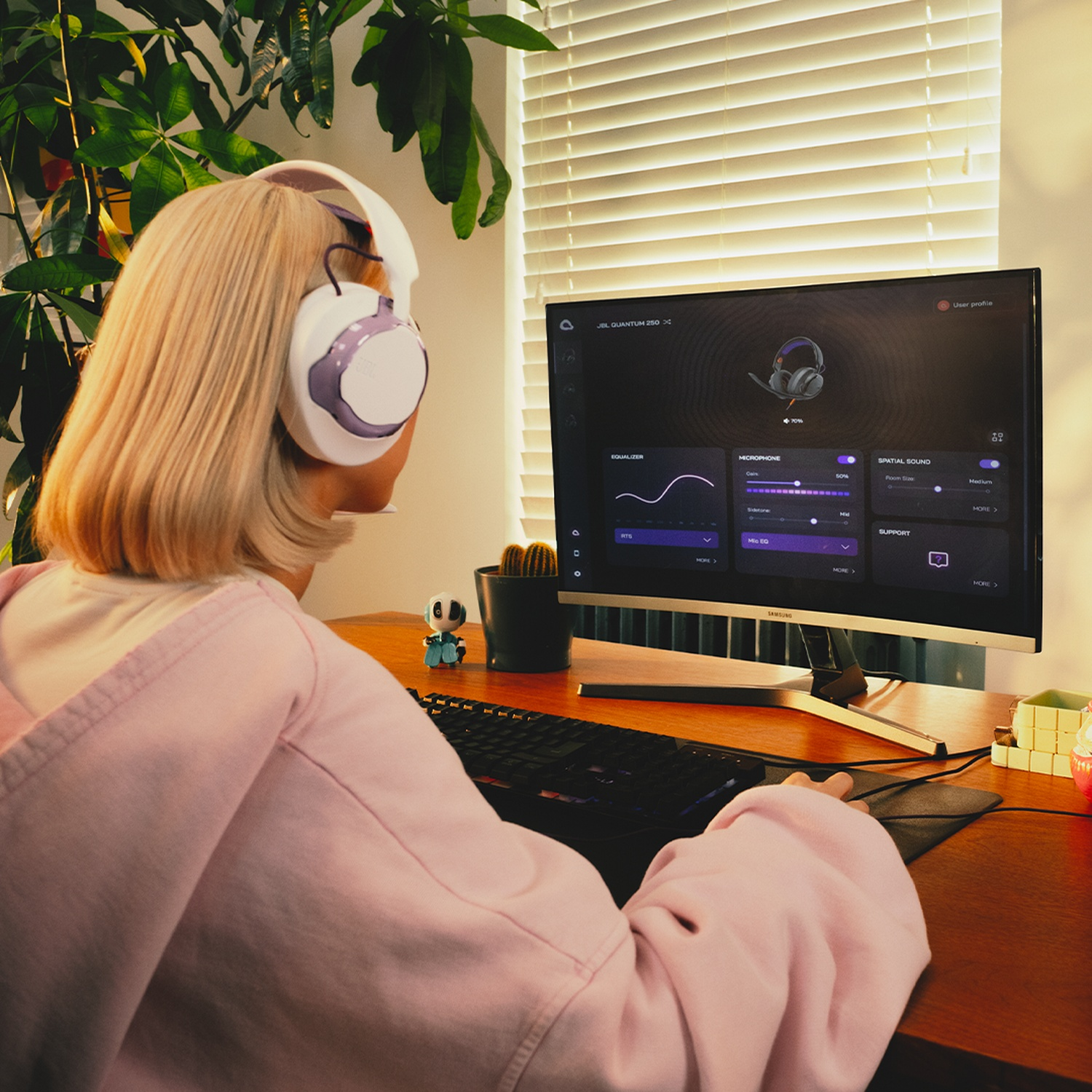 Une personne avec un casque utilise un ordinateur. L'écran affiche les paramètres audio. Il y a un clavier, une souris et une plante en arrière-plan.