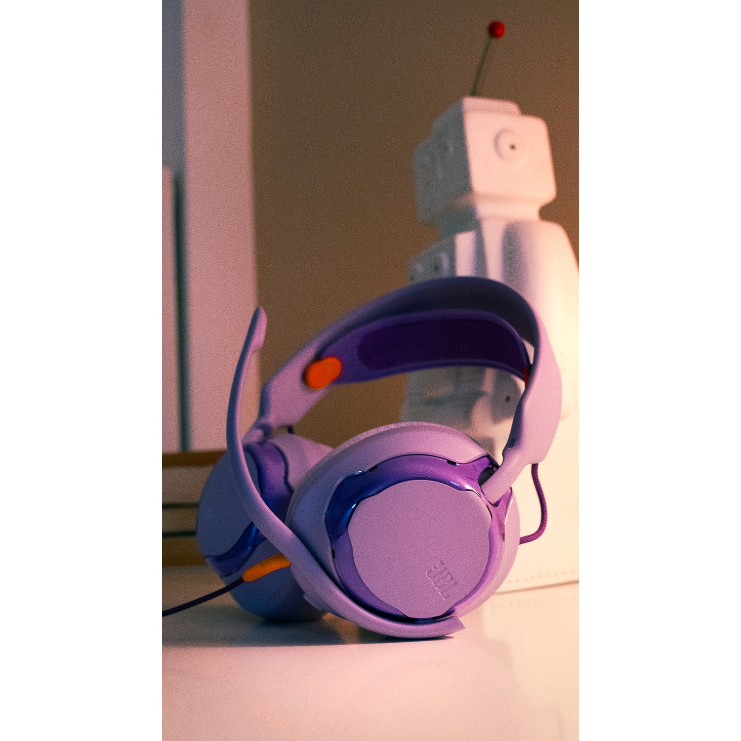 Purple JBL headphones with a robot in the background. Headphones are on a white surface. Robot has a red antenna.