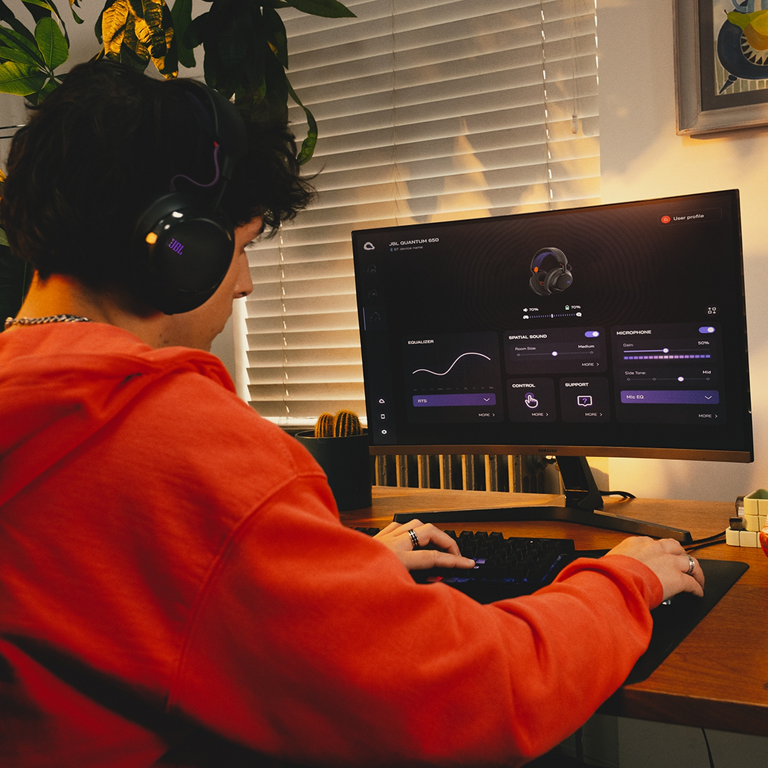 Une personne portant un casque, utilisant un ordinateur avec un moniteur affichant les paramètres audio, dans une pièce avec des plantes.