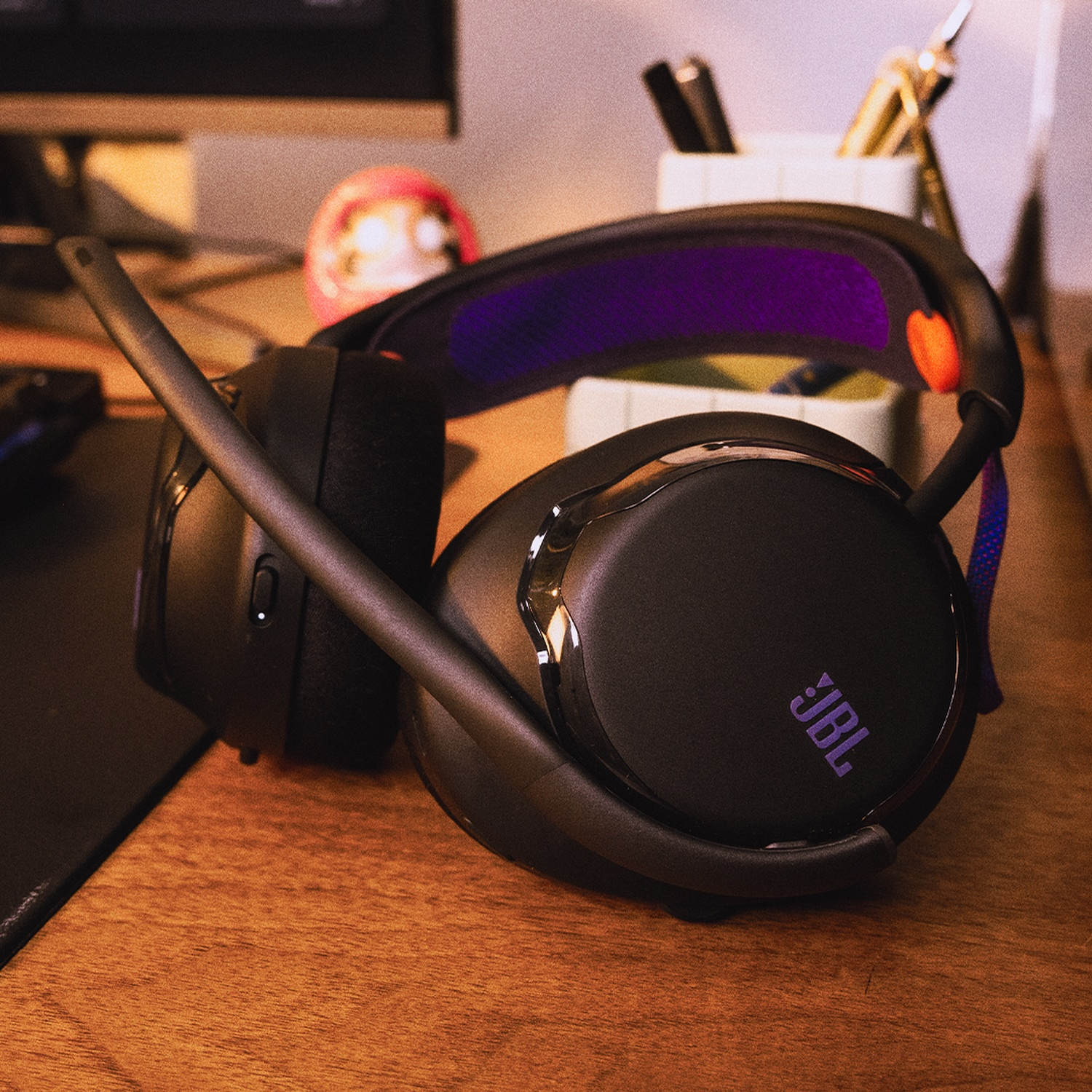 Casque JBL noir sur un bureau en bois. Le casque a un microphone. D'autres éléments sont visibles en arrière-plan.