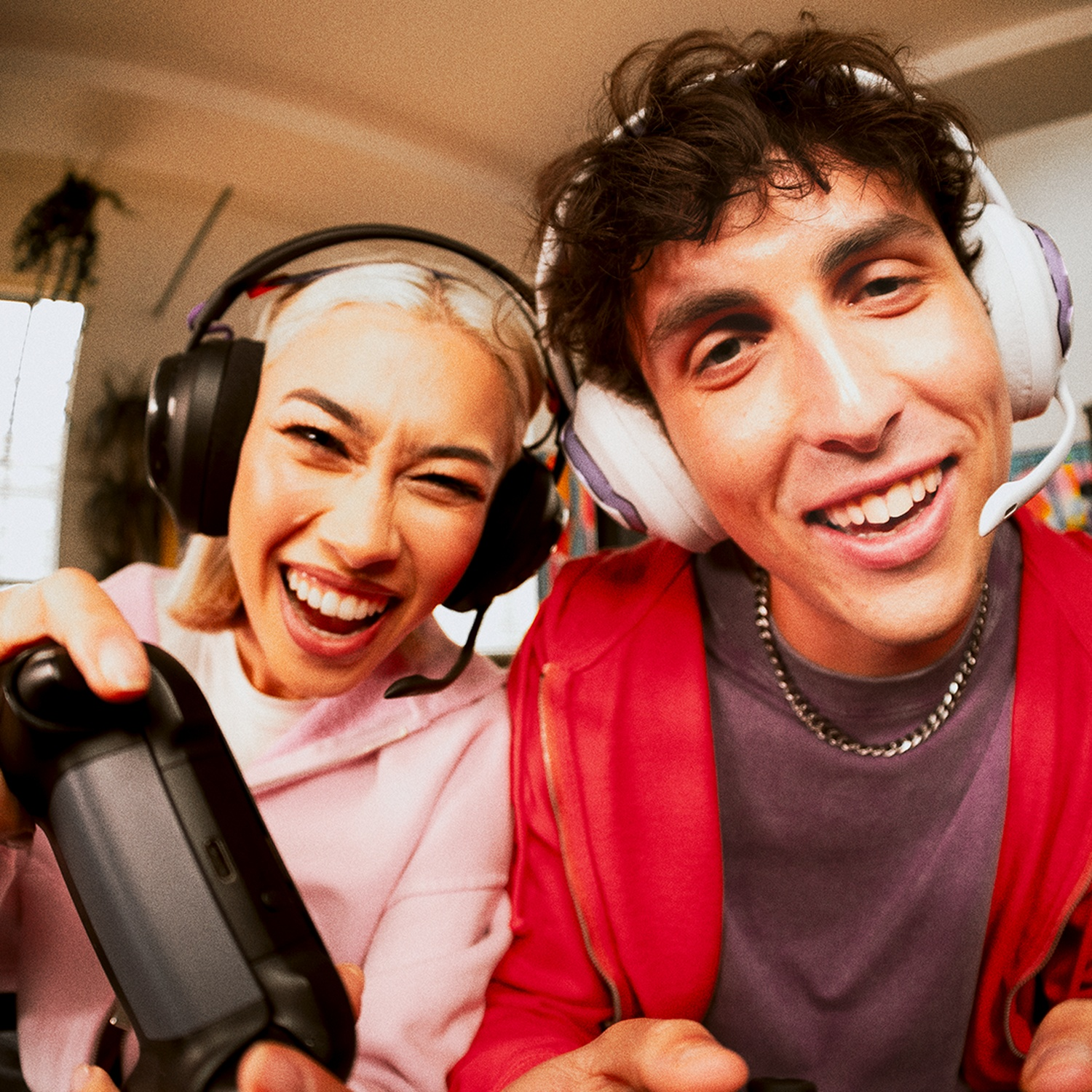 Deux personnes portant des casques, souriant tout en tenant des manettes. L'une en rose, l'autre en rouge, jouant à un jeu vidéo.