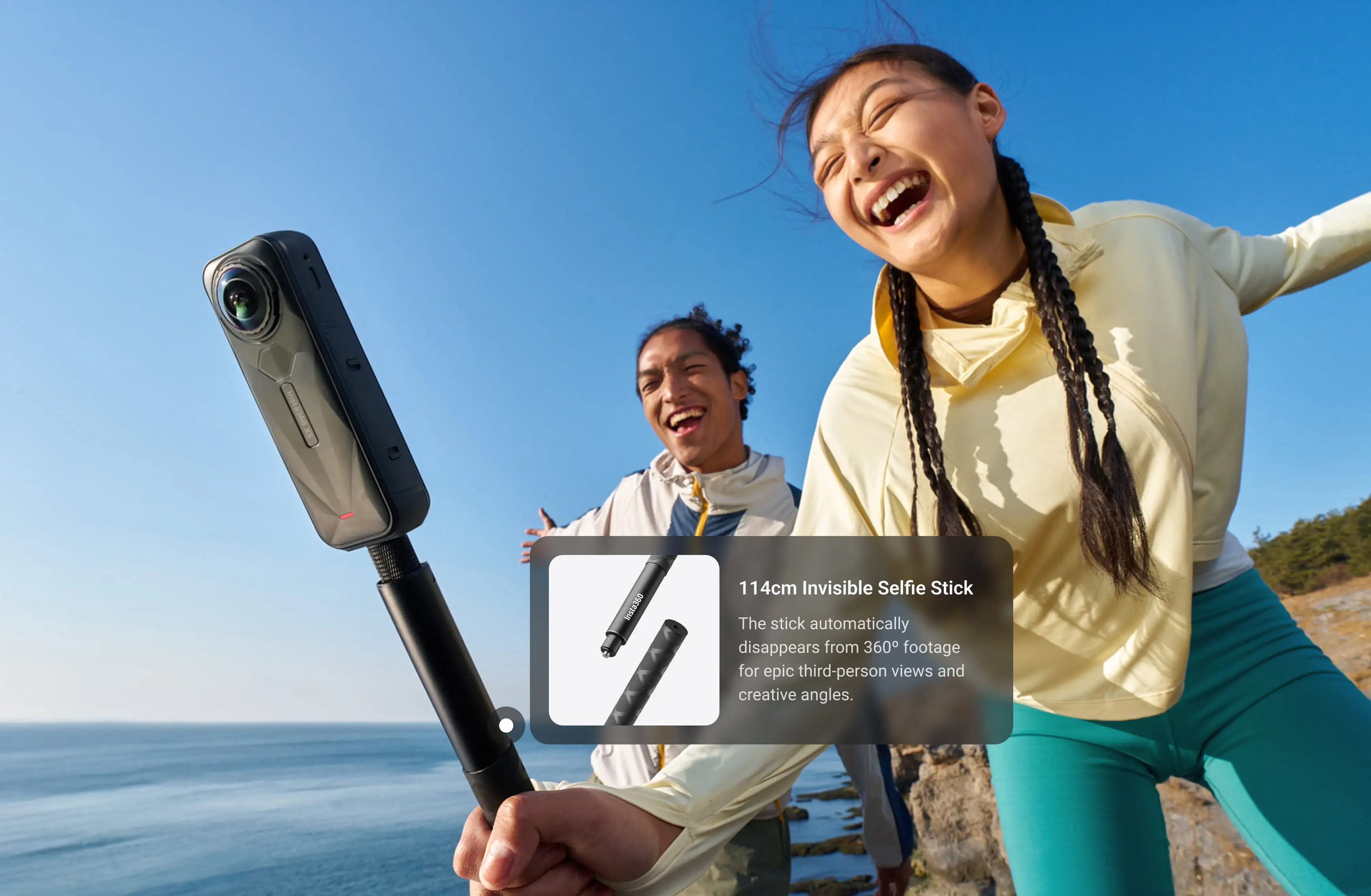 Zwei lachende Personen im Freien. Einer hält einen Selfie-Stick mit Kamera. Klarer blauer Himmel im Hintergrund.