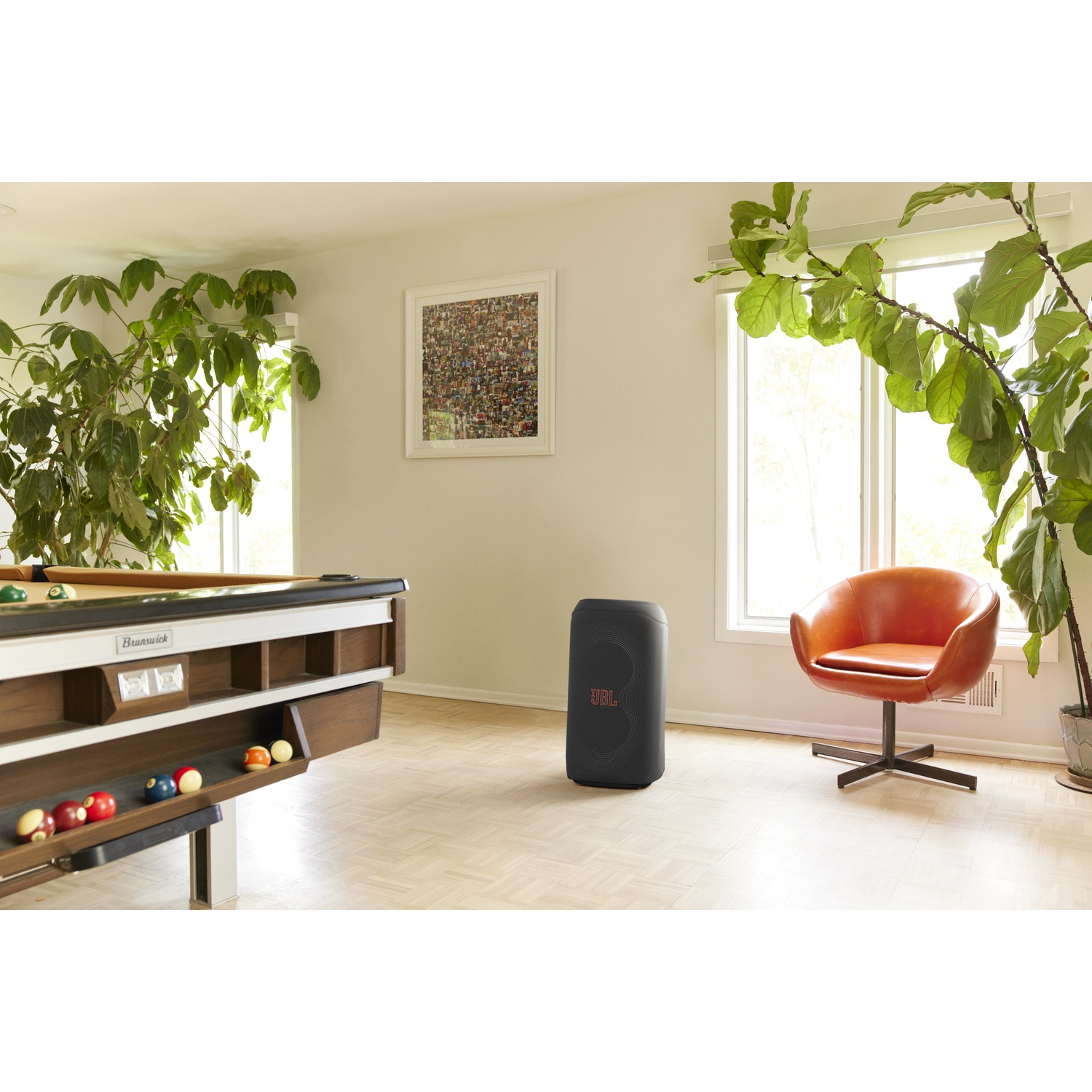 Een kamer met een pooltafel, een luidspreker, een oranje stoel, planten en een ingelijste foto. De vloer is licht hout.