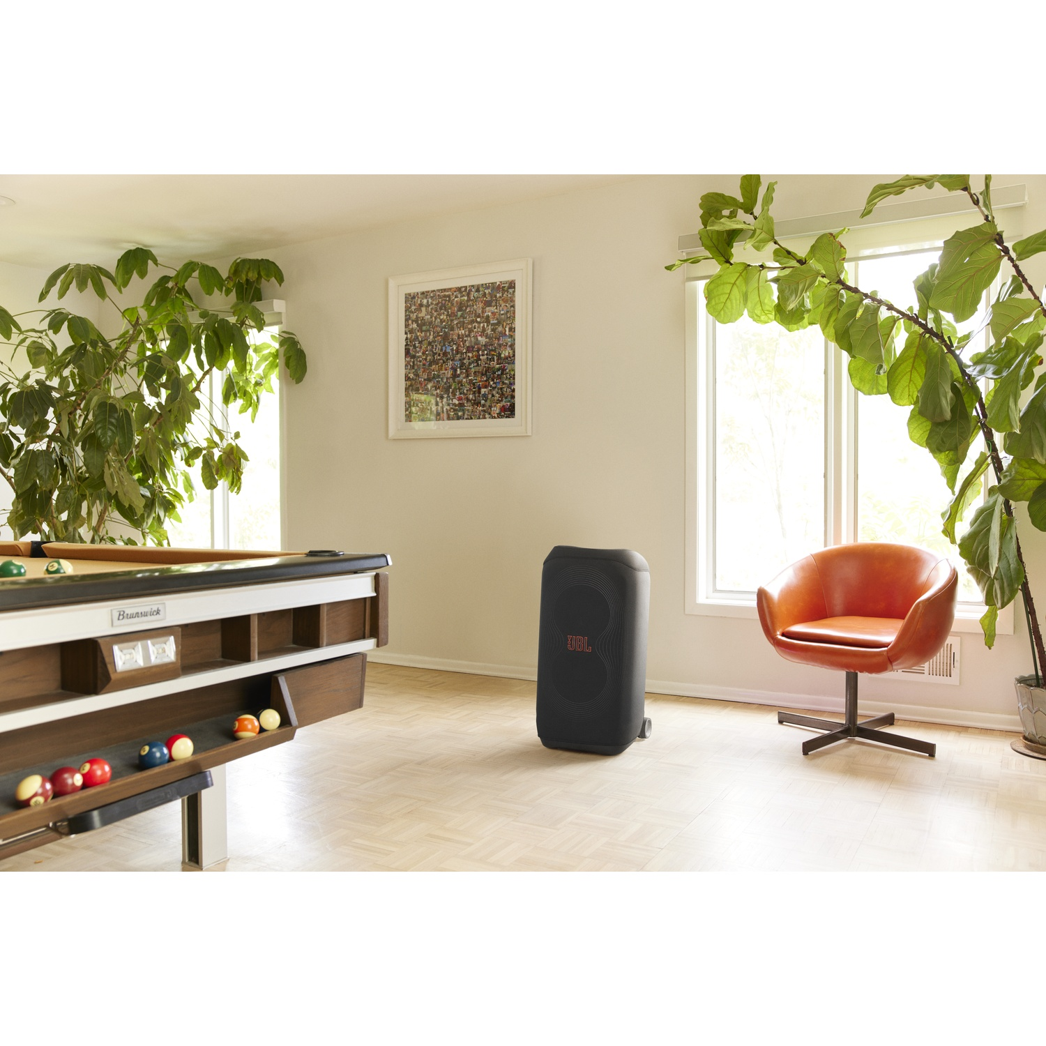 Een woonkamer met een pooltafel, een luidspreker en een oranje stoel. Planten en ramen zijn ook zichtbaar.