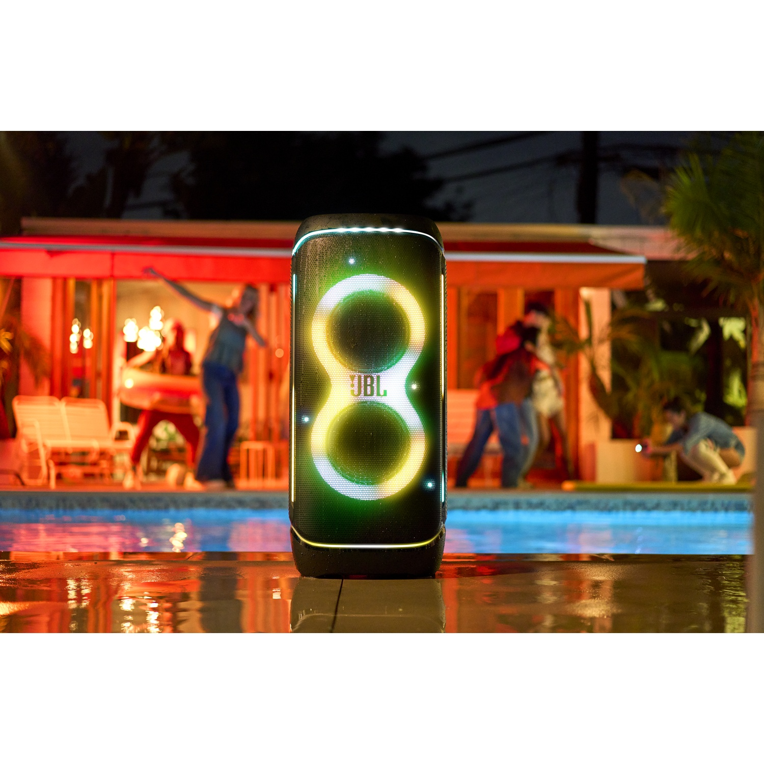 Een JBL-luidspreker met een oplichtend 8-ontwerp staat voor een zwembad. Mensen zijn op de achtergrond en de scène is verlicht.