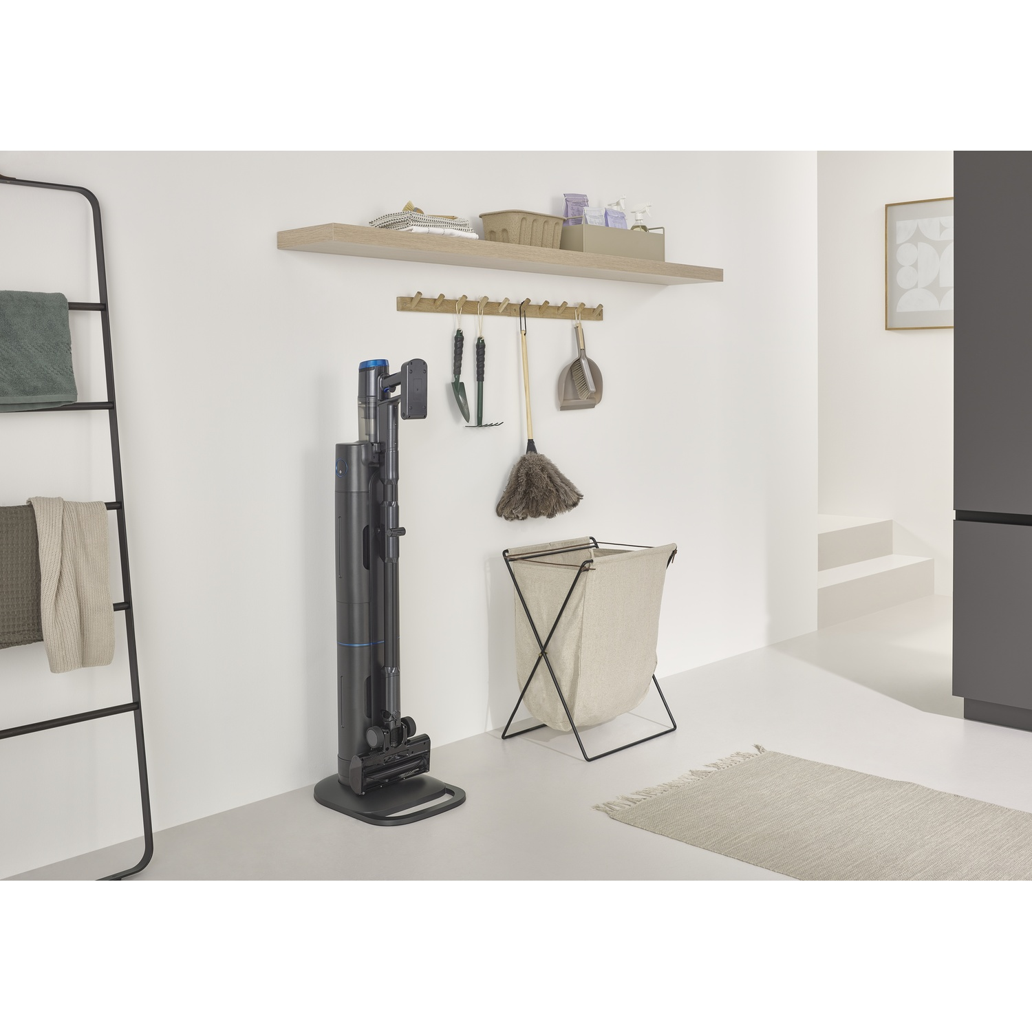 Un interno moderno con aspirapolvere, prodotti per la pulizia, un cesto per il bucato e un tappeto. I colori neutri dominano.