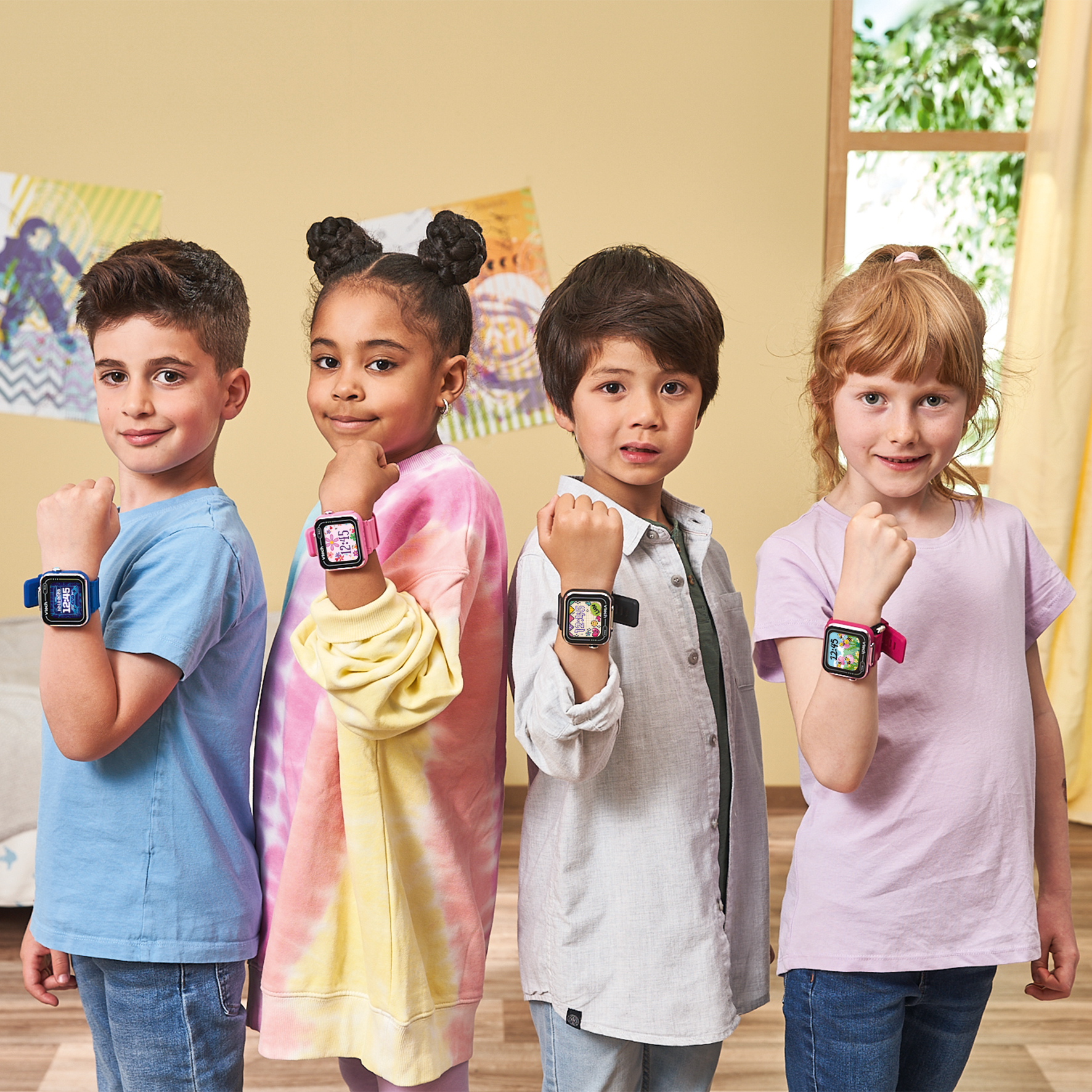 Cuatro niños con smartwatches posan con los puños en alto. Están dentro cerca de una ventana. El fondo es amarillo claro.