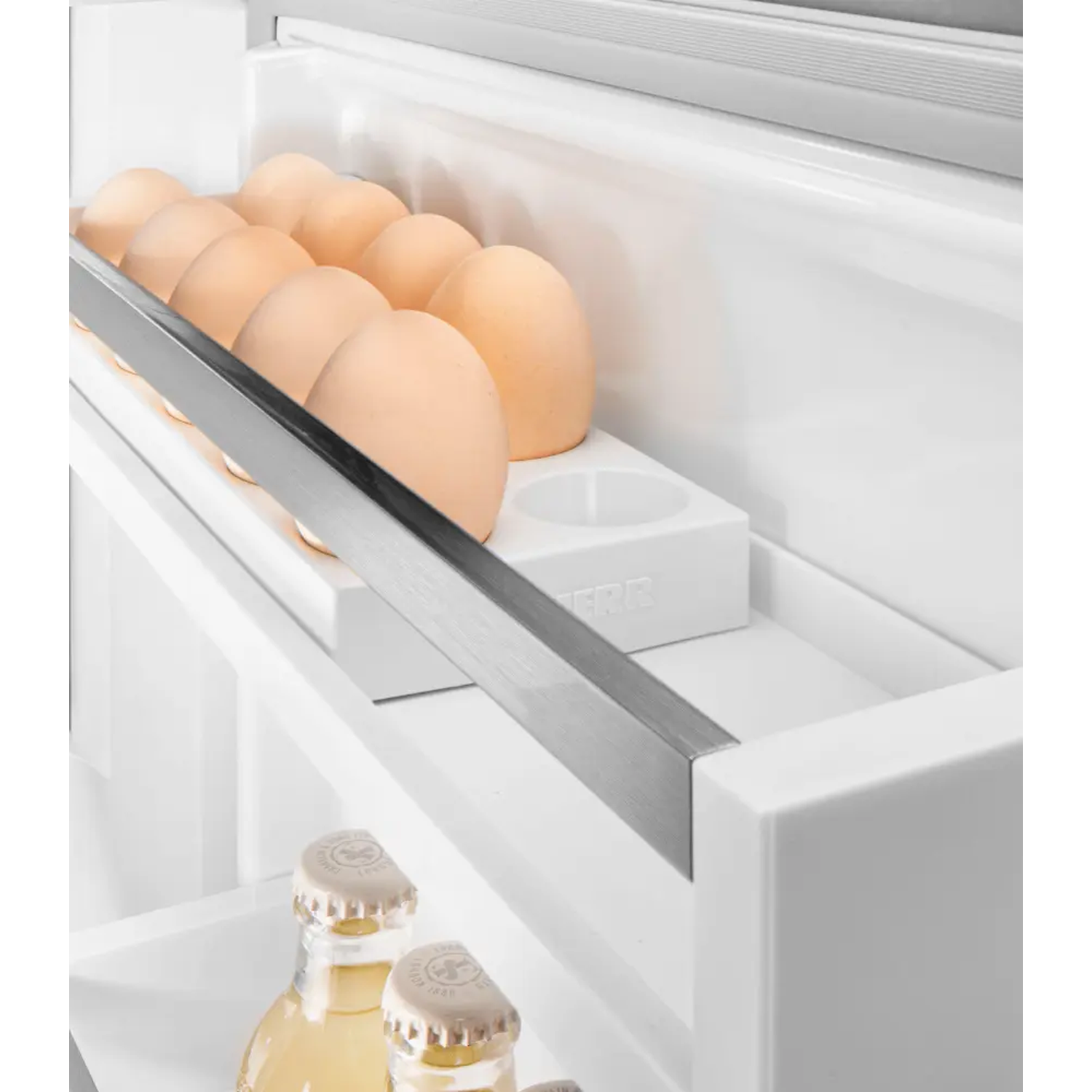 In een koelkast: eieren in een houder, bierflesjes beneden. Witte planken en muren. Eieren zijn lichtbruin.