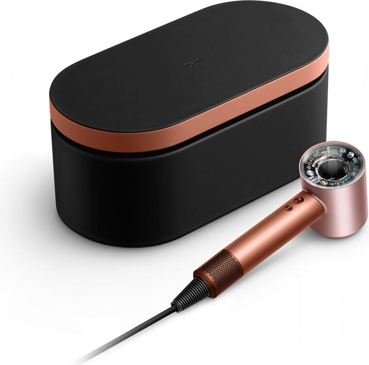 Czarna i miedziana suszarka do włosów Dyson oraz jej etui na białej powierzchni. Suszarka jest w kolorze różowego złota.