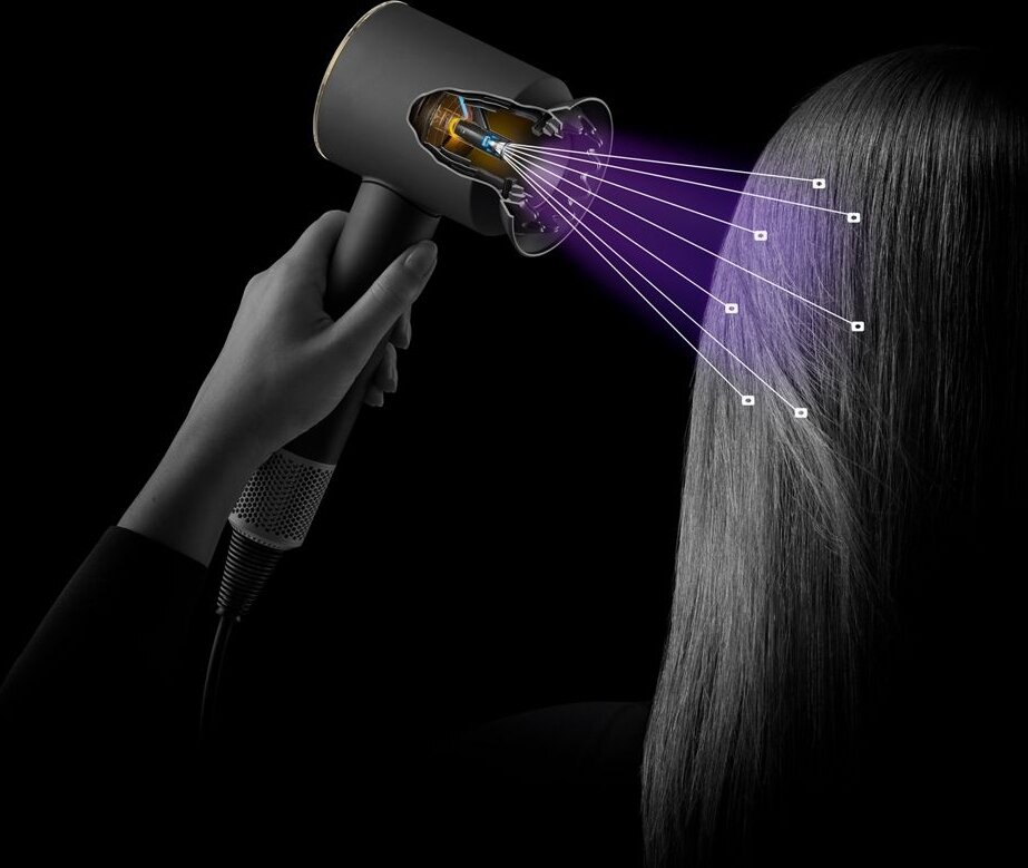 Osoba używa czarnej suszarki do włosów. Suszarka emituje fioletowe wiązki na włosy, ilustrując jej działanie.