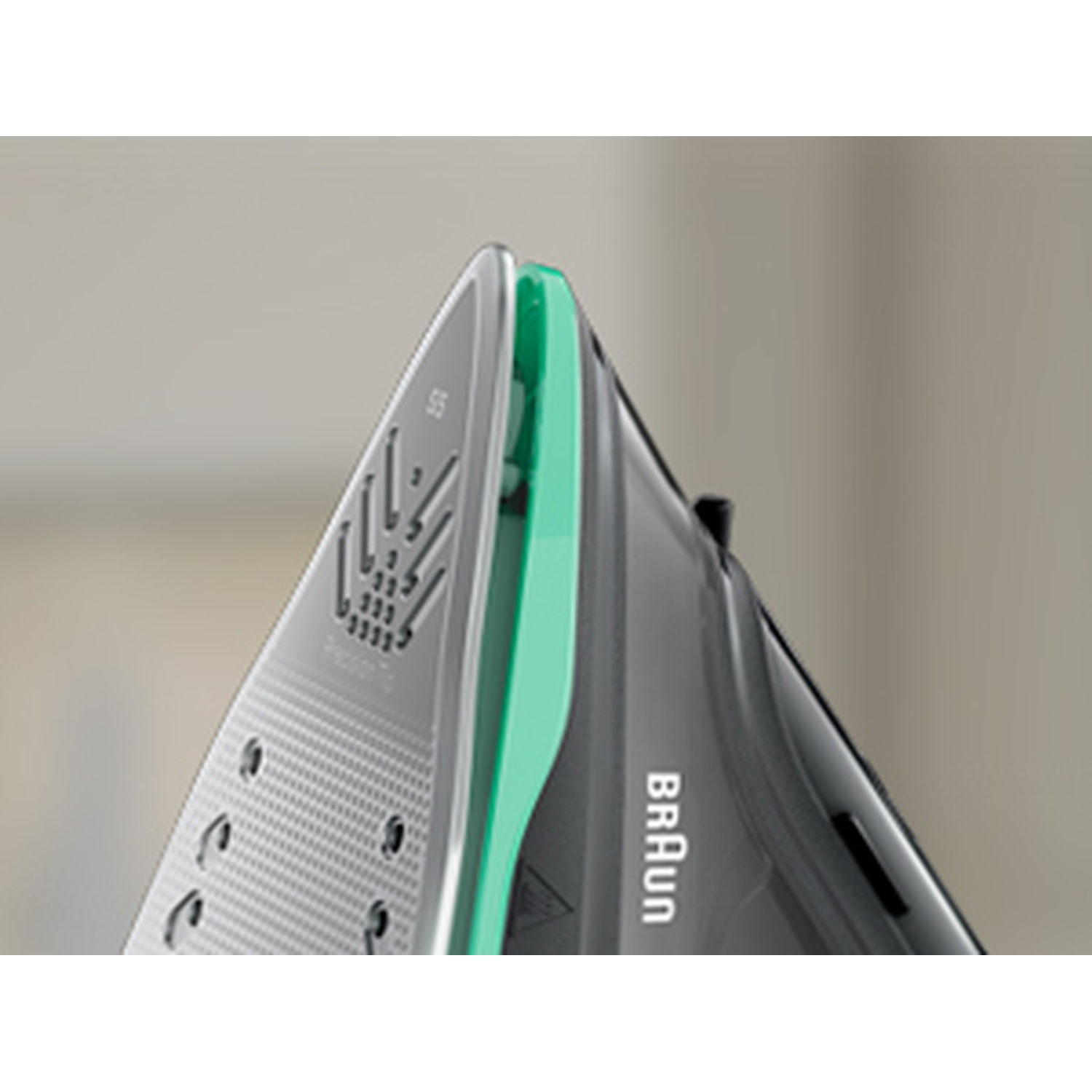 Primo piano di un ferro da stiro Braun. Piastra argentata con dettagli verdi. Manico nero con logo Braun. Sfondo sfocato.
