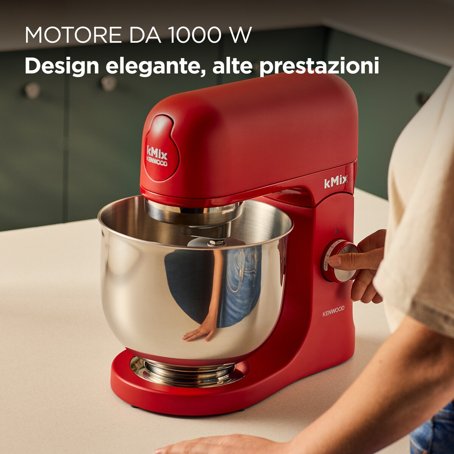 Un mixer planetario Kenwood kMix rosso con una ciotola in acciaio inossidabile. Una mano sta girando la manopola. Il testo recita 'MOTORE DA 1000 W'.