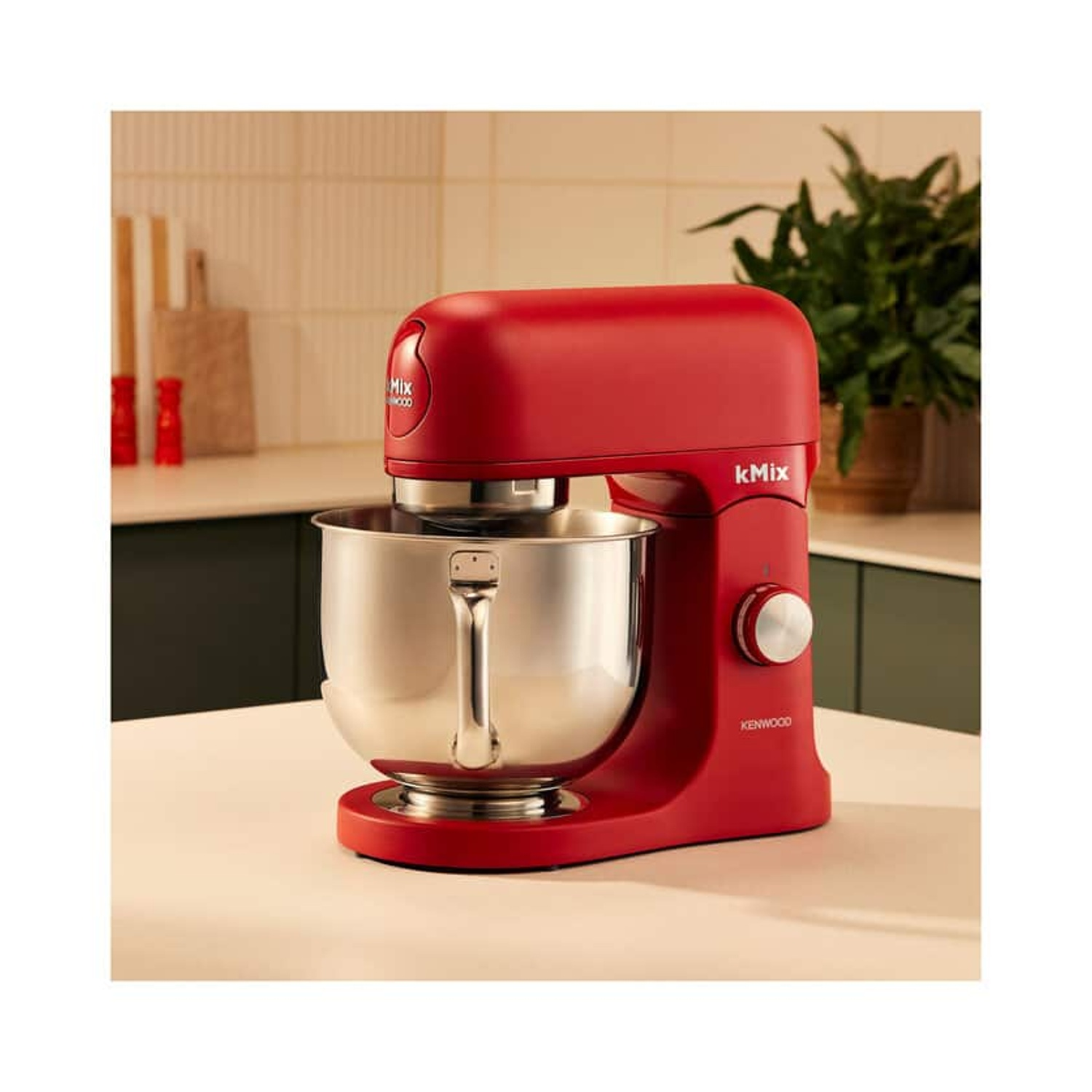 Un robot da cucina rosso Kenwood kMix con una ciotola in acciaio inossidabile. Si trova su un piano di lavoro color crema in una cucina.
