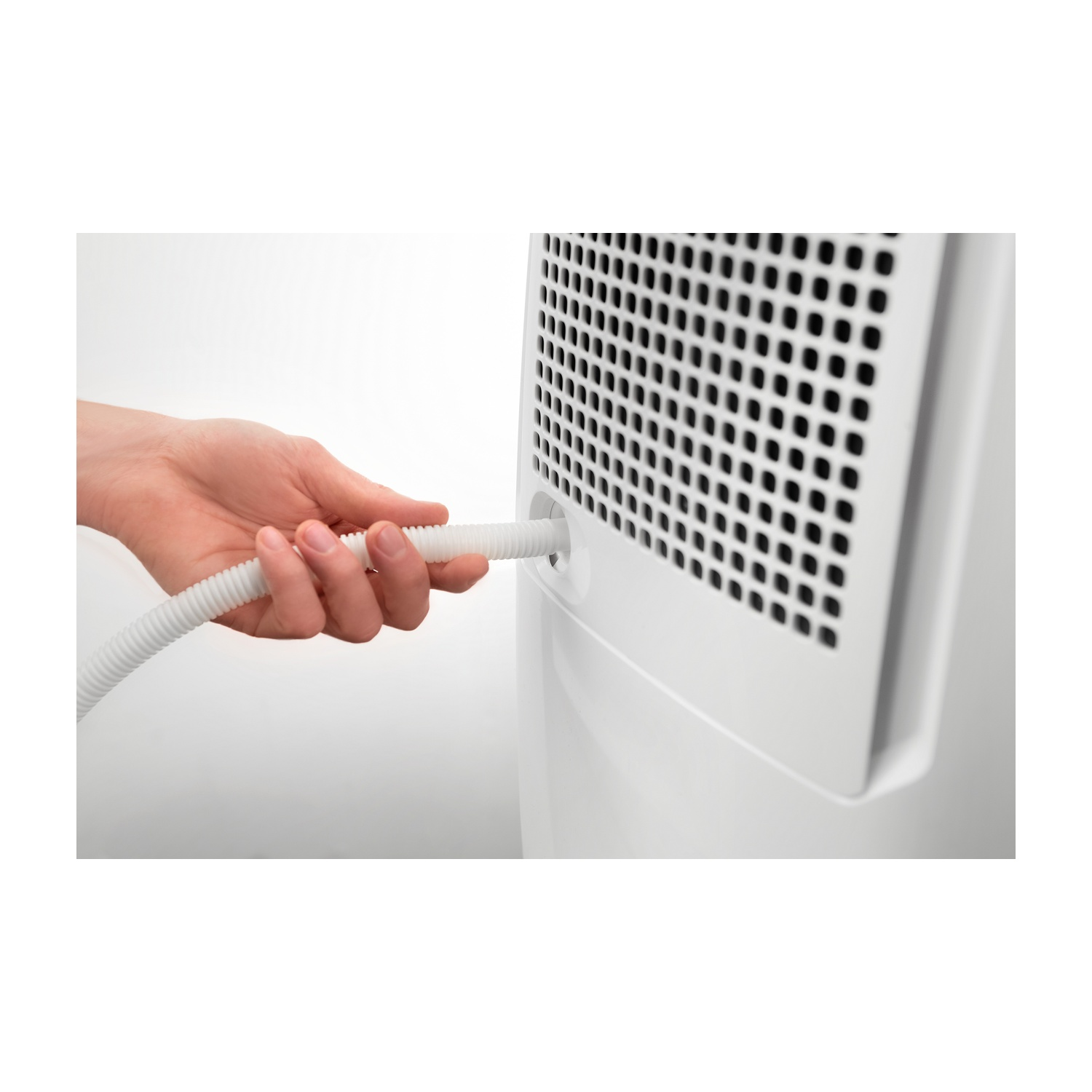 Una mano inserisce un tubo bianco ondulato in un elettrodomestico bianco. L'apparecchio ha un pannello nero perforato.
