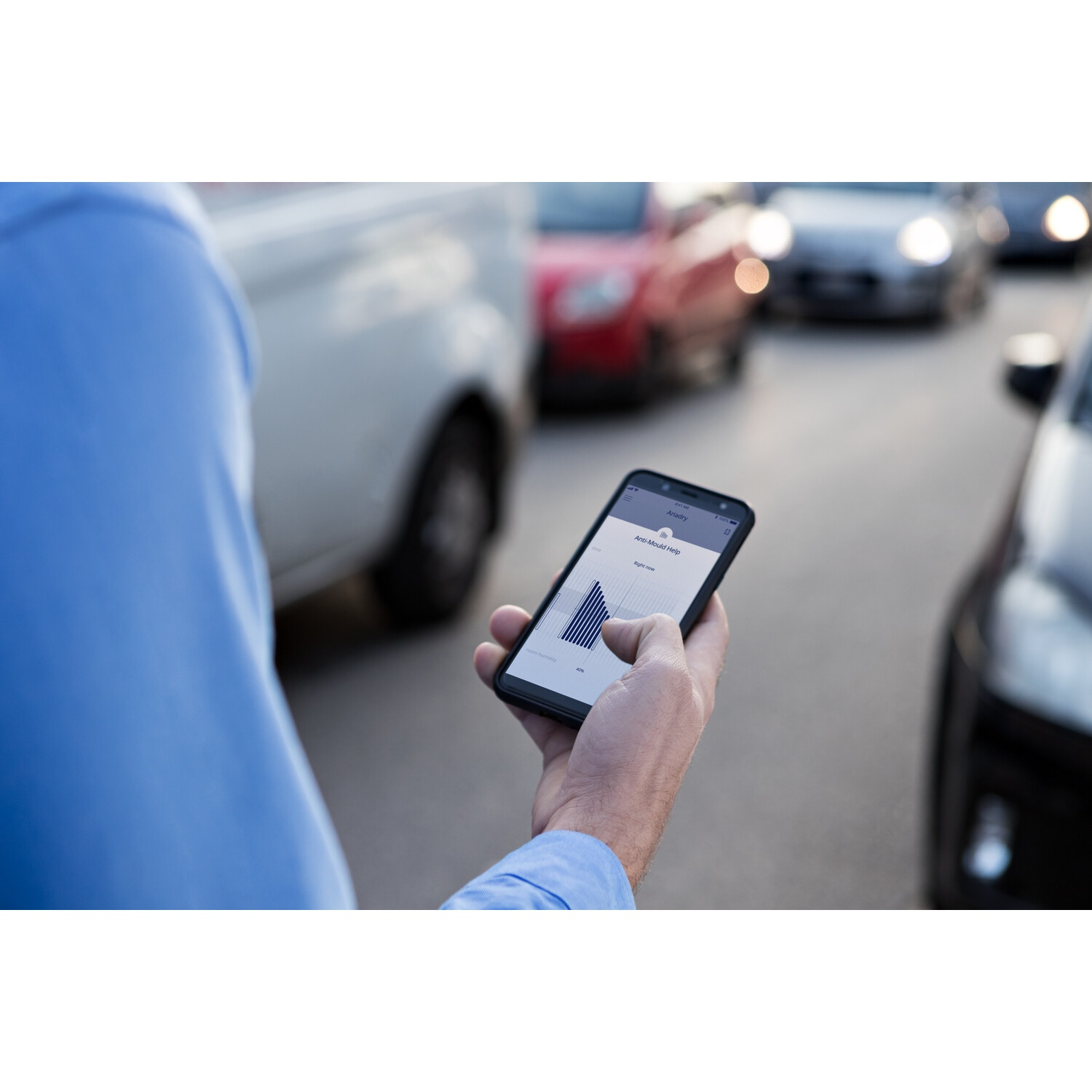 Una persona tiene in mano uno smartphone che mostra un grafico, forse per monitorare l'attività, con auto sullo sfondo.
