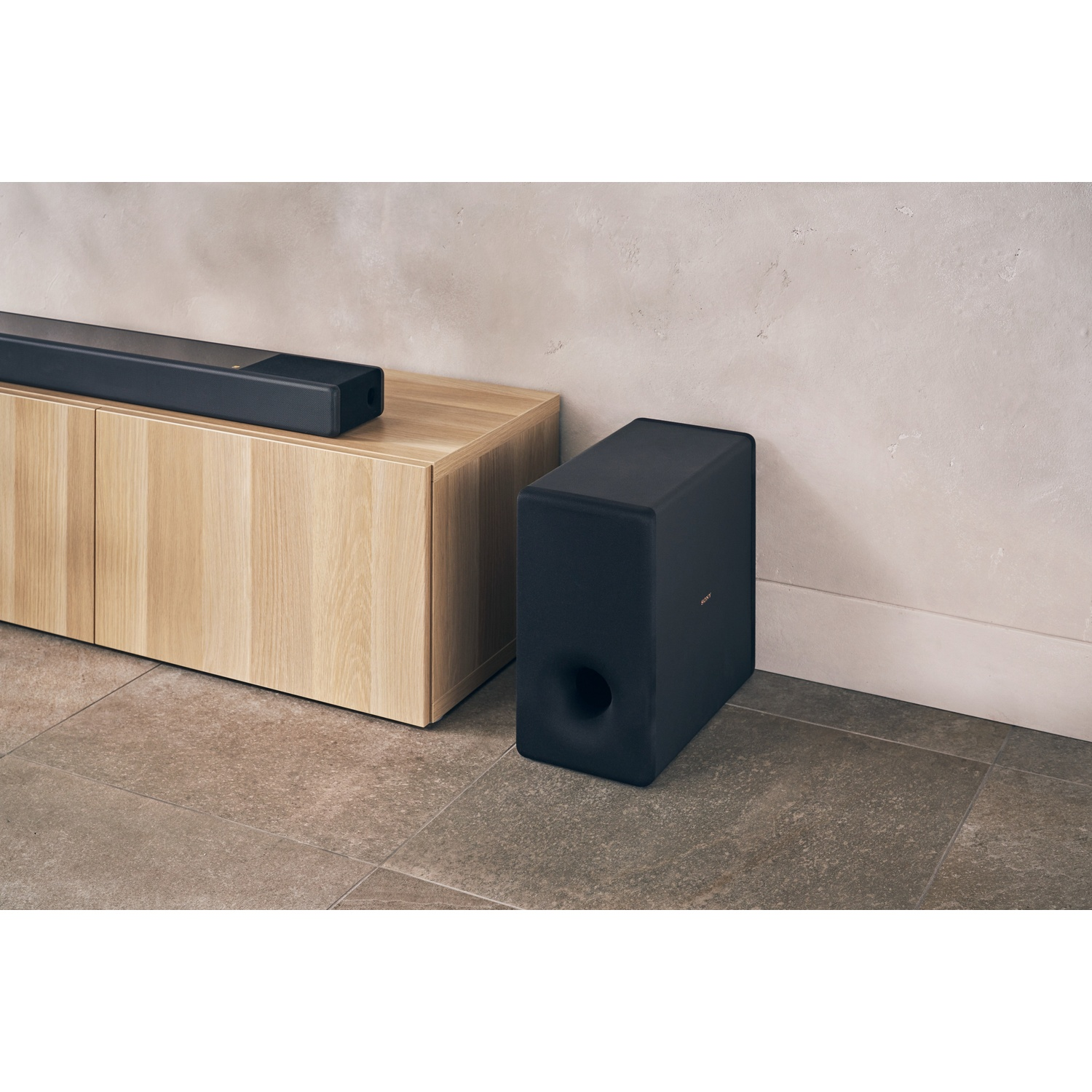 Una soundbar e un subwoofer neri sono su un mobile in legno e un pavimento piastrellato. Lo sfondo è una parete strutturata.