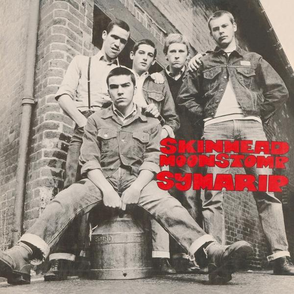 Fünf Männer in Jeans und Jacken posieren an einer Backsteinmauer, die Worte 'Skinhead Moonstomp Symarip' sind rot.