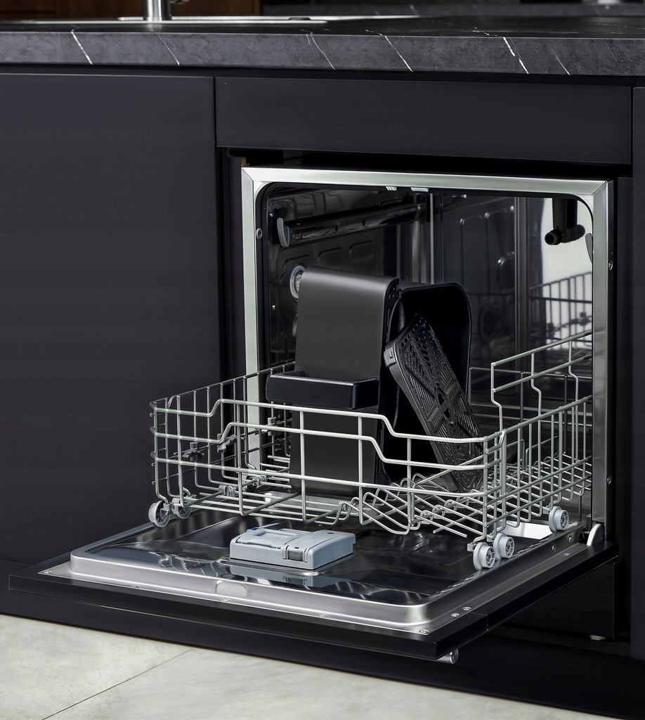 Otwarta zmywarka z czarnym wnętrzem. Zawiera czarne pojemniki i szary filtr. Widoczny stelaż ze stali nierdzewnej.