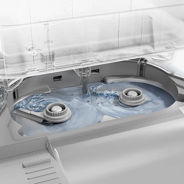 Wnętrze zmywarki. Woda tryska z dyszy na obracające się ramiona spryskiwaczy. Wnętrze maszyny jest szare i przezroczyste.