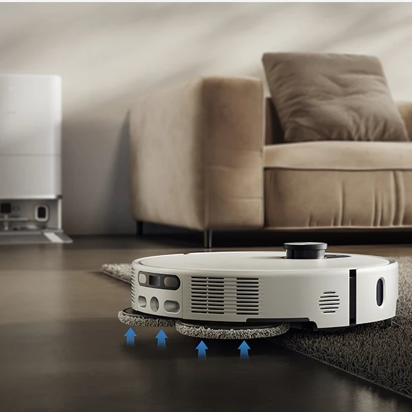 Biały robot sprzątający czyści pokój. W tle kanapa i urządzenie.