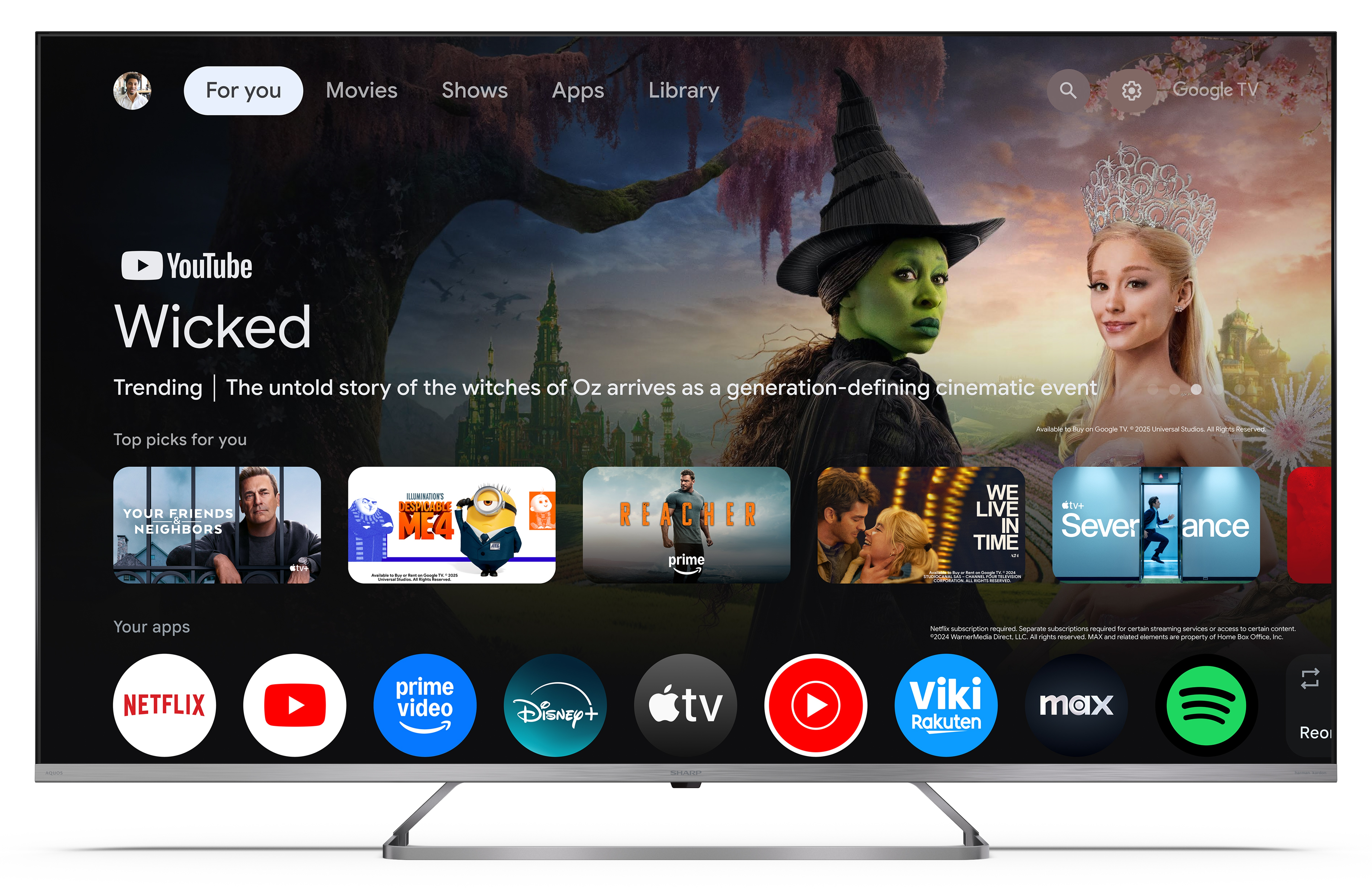 Ekran telewizora wyświetla interfejs Google TV. Prominentna promocja Wicked z zielonoskórą czarownicą i Arianą Grande.