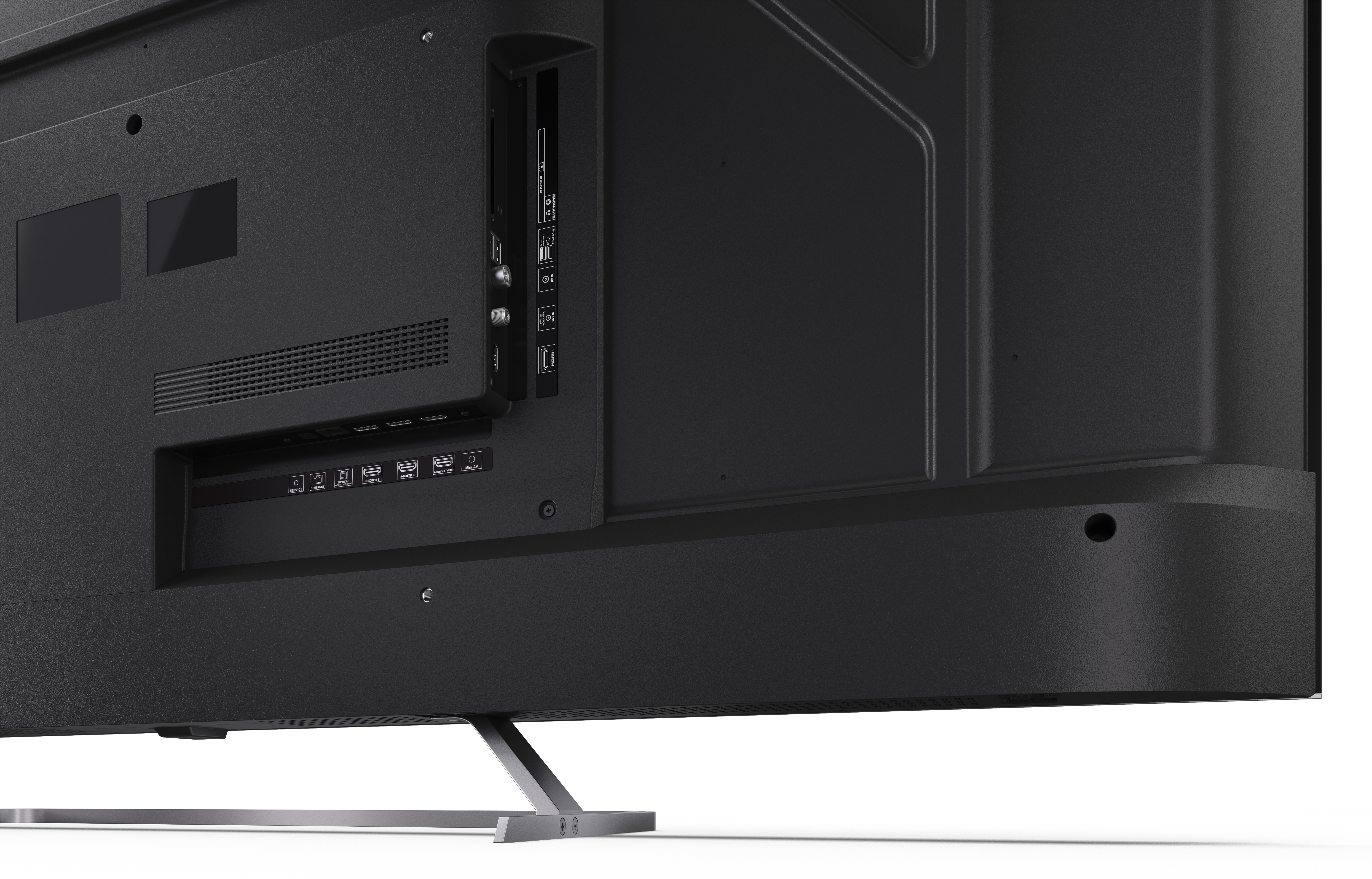 Widoczny tył czarnego telewizora z różnymi portami i srebrną podstawą. Telewizor stoi na białej powierzchni.
