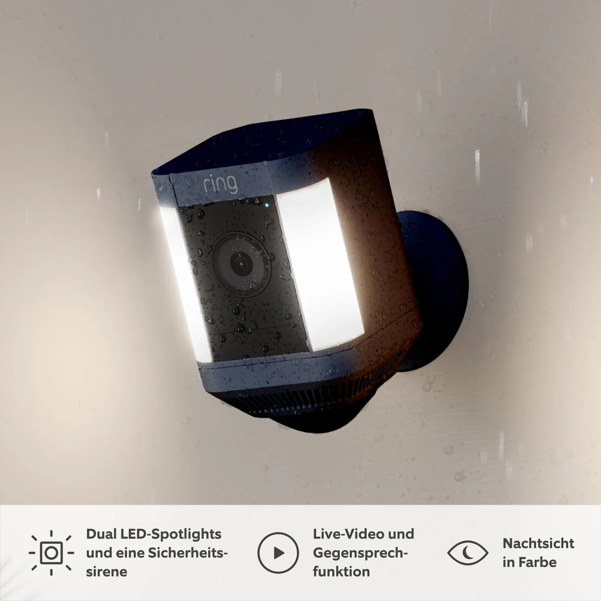 Eine schwarze Ring-Sicherheitskamera mit hellen Lichtern, an einer Wand montiert. Regentropfen sind sichtbar. Text erwähnt LED-Scheinwerfer und Nachtsicht.