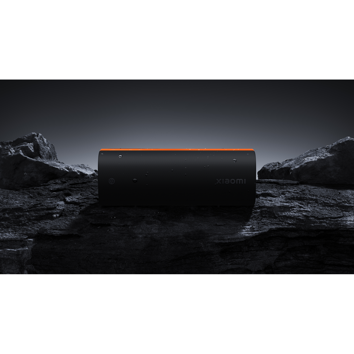 A black speaker with orange accents rests on dark rocks. The speaker has the Xiaomi logo. The background is a gradient.