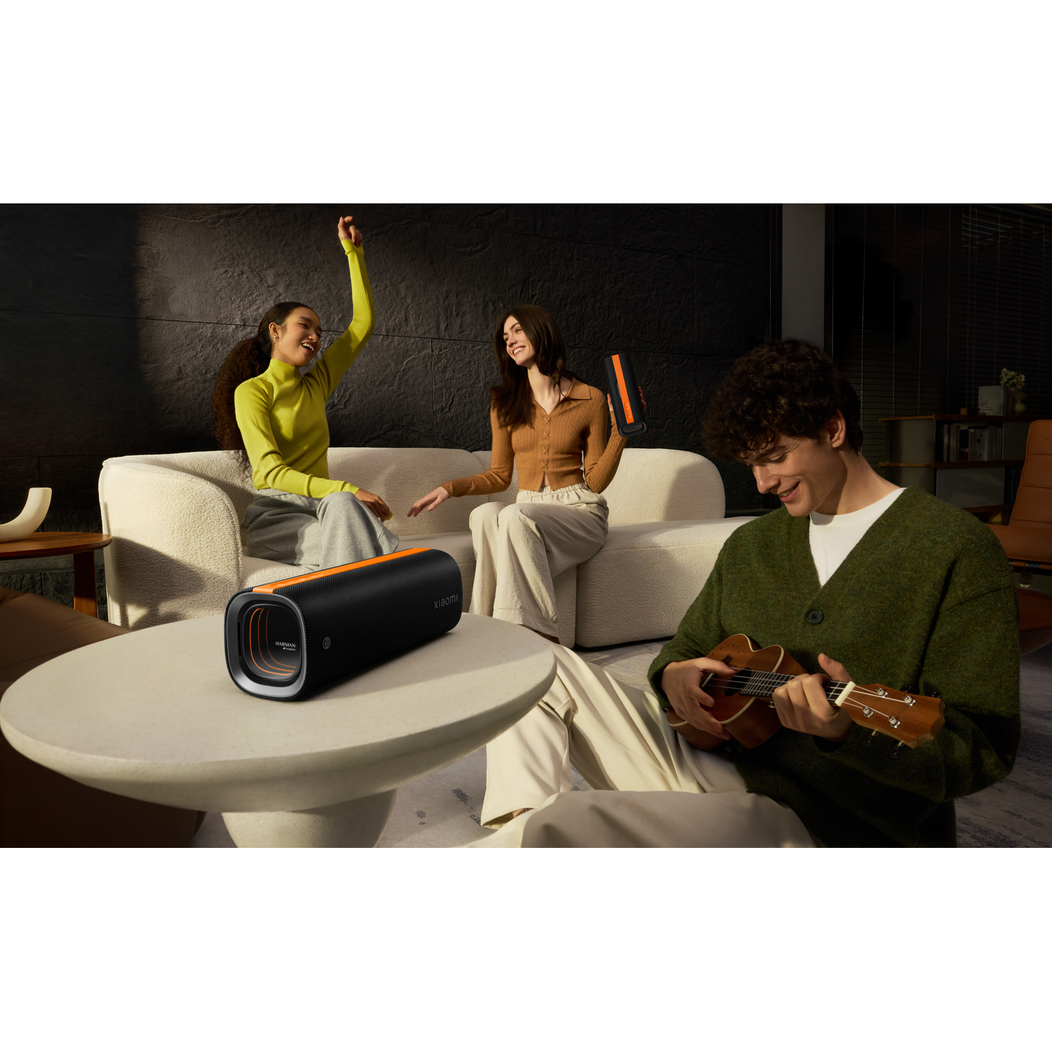 Three people in a living room, one playing a ukulele. A black speaker sits on a table. People are laughing and having fun.