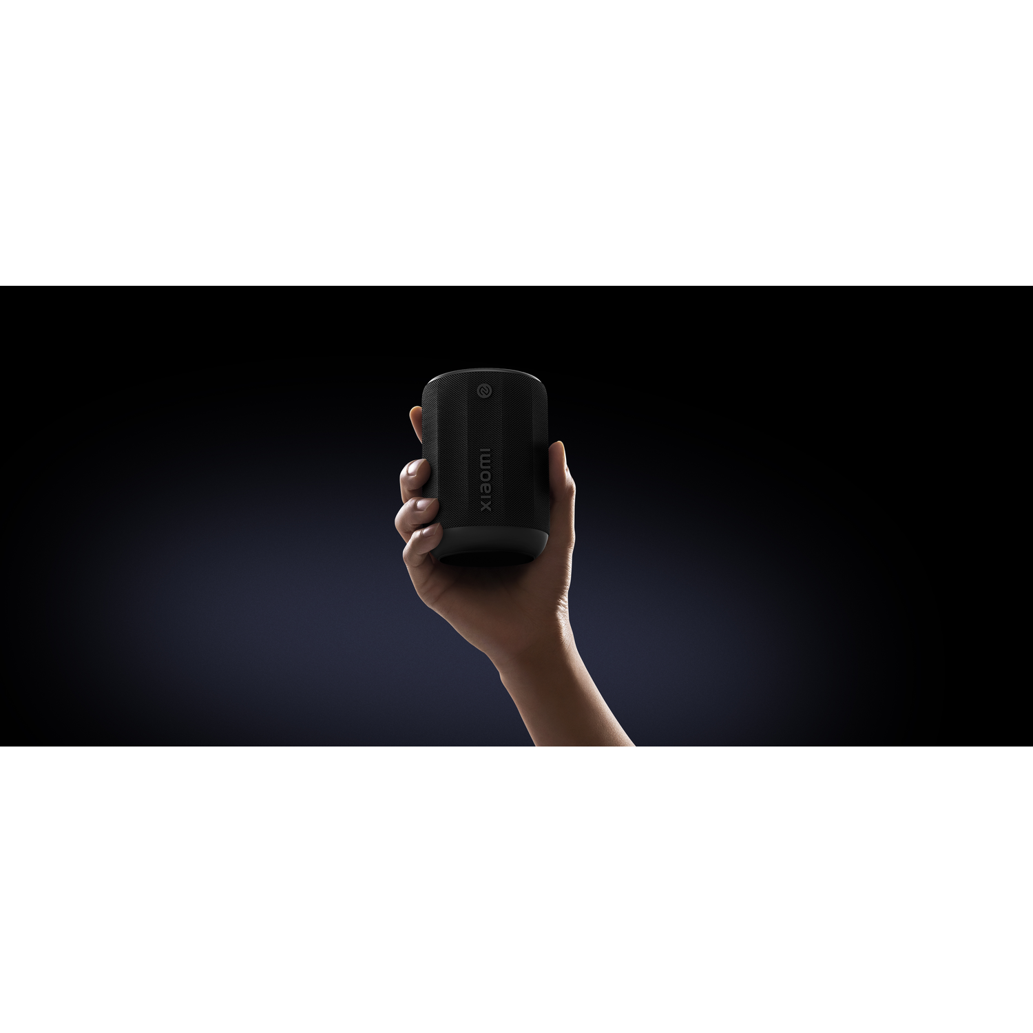A hand holding a black Xiaomi speaker. The background is dark blue. The speaker has the Xiaomi logo.