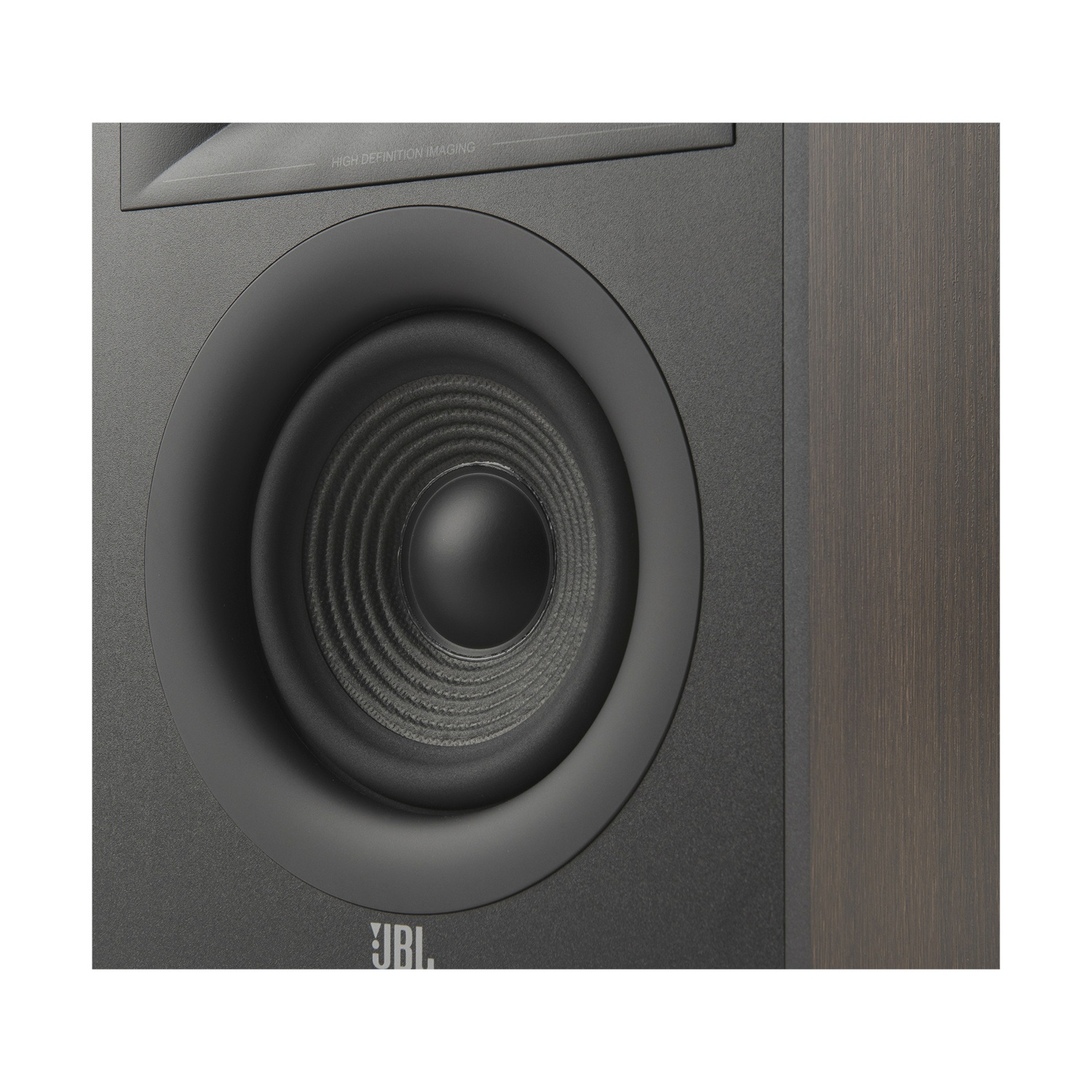 Primo piano di un altoparlante JBL. L'altoparlante ha un woofer nero con un bordo grigio scuro e un cabinet nero strutturato.