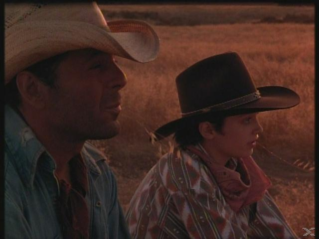 Két cowboy kalapban jobbra néz. Az egyik szalmakalapot, a másik fekete kalapot visel. Száraz fű közelében ülnek. Lágy fény.