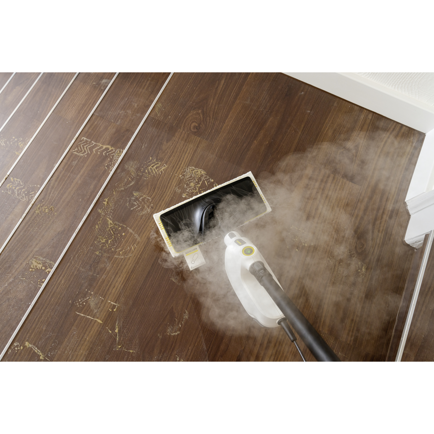 Steam cleaner on a wooden floor with footprints. Steam is emitted. The floor is brown, and the cleaner is white and black.